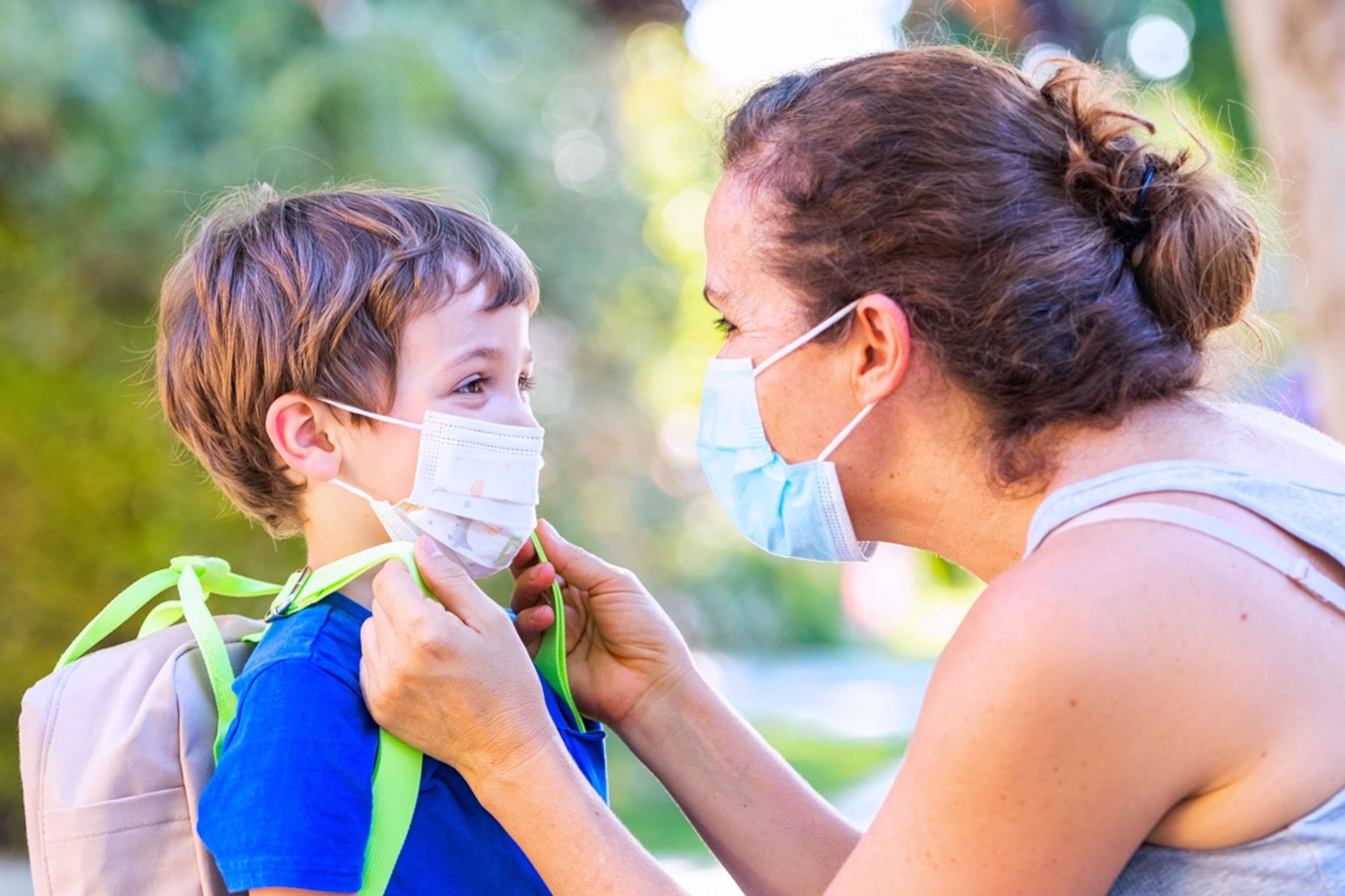 Mature woman and son face to face she is putting him on a protective face mask.