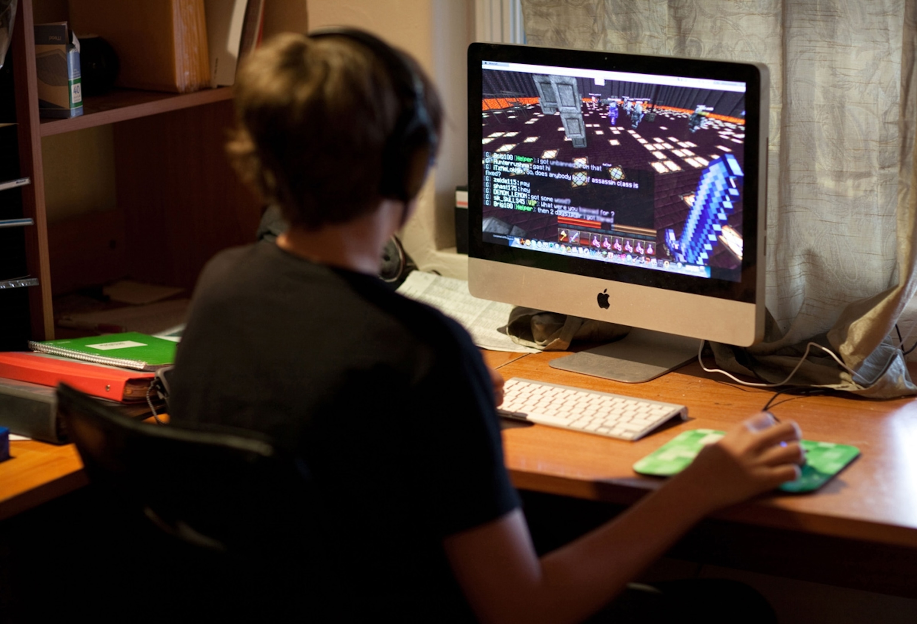 Thirteen year old boy playing the popular Minecraft video game at home, wearing headphones.