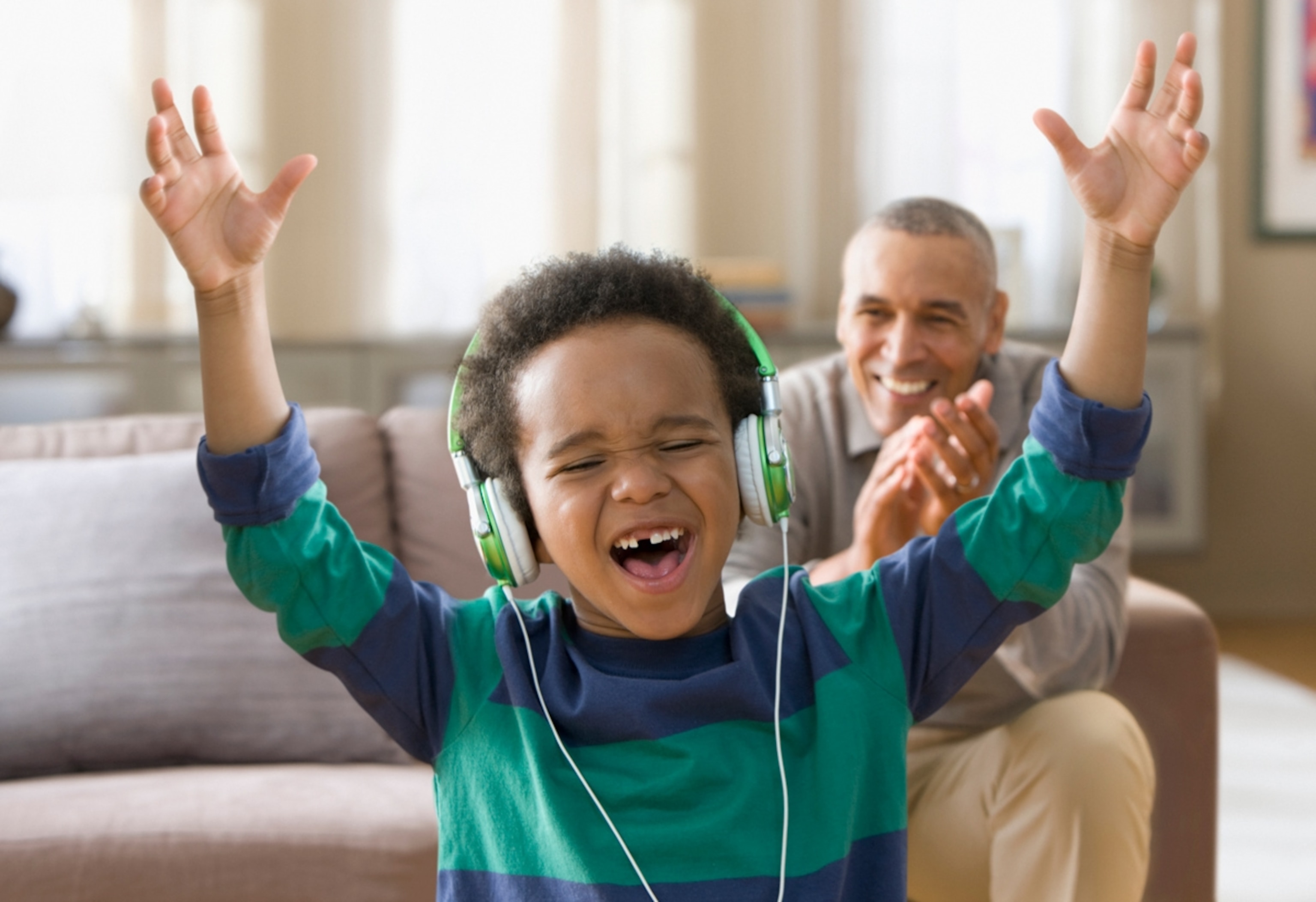 Grandfather watching grandson listening to music on headphones.