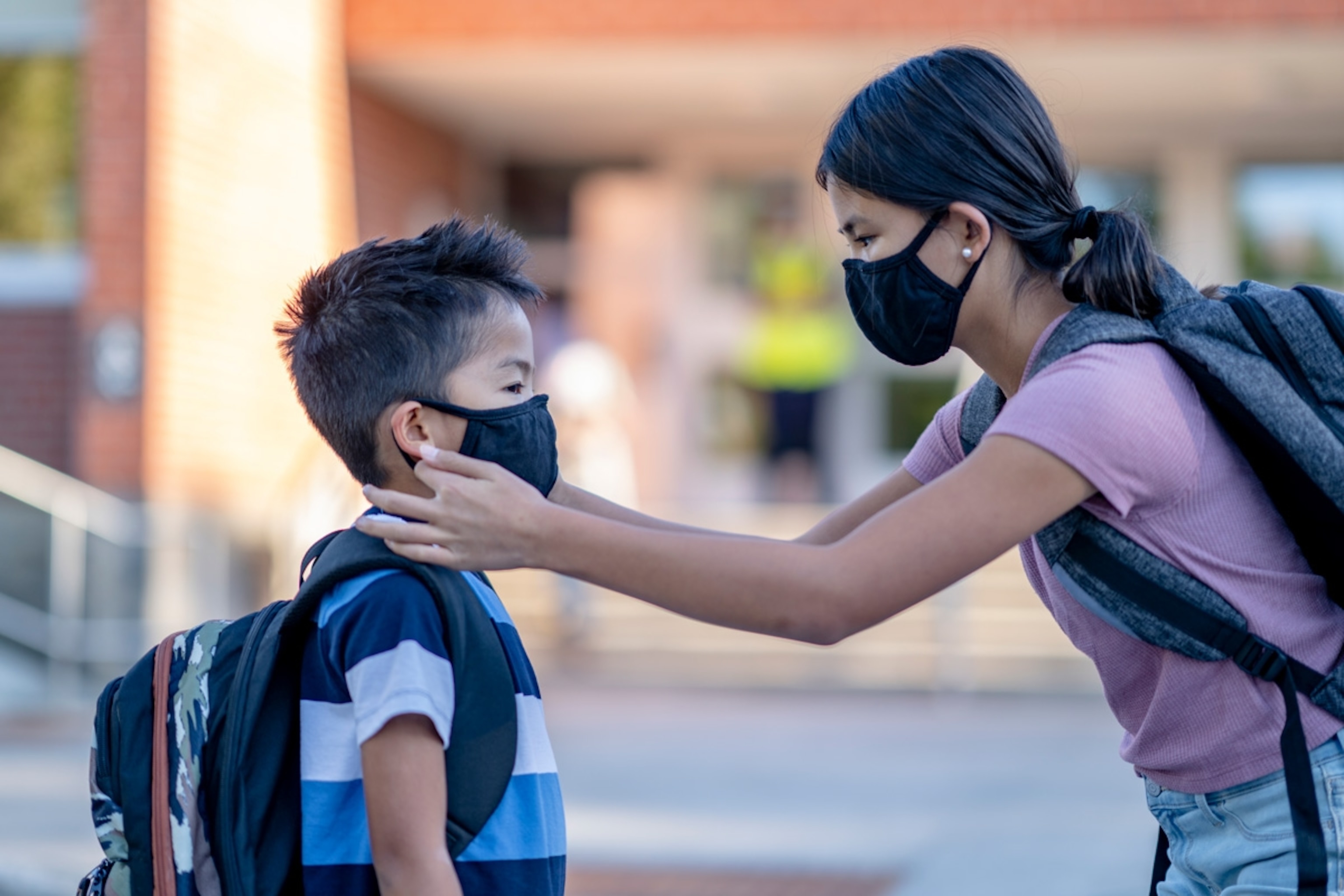 Sister helping younger brother adjust his face mask before going into school.
