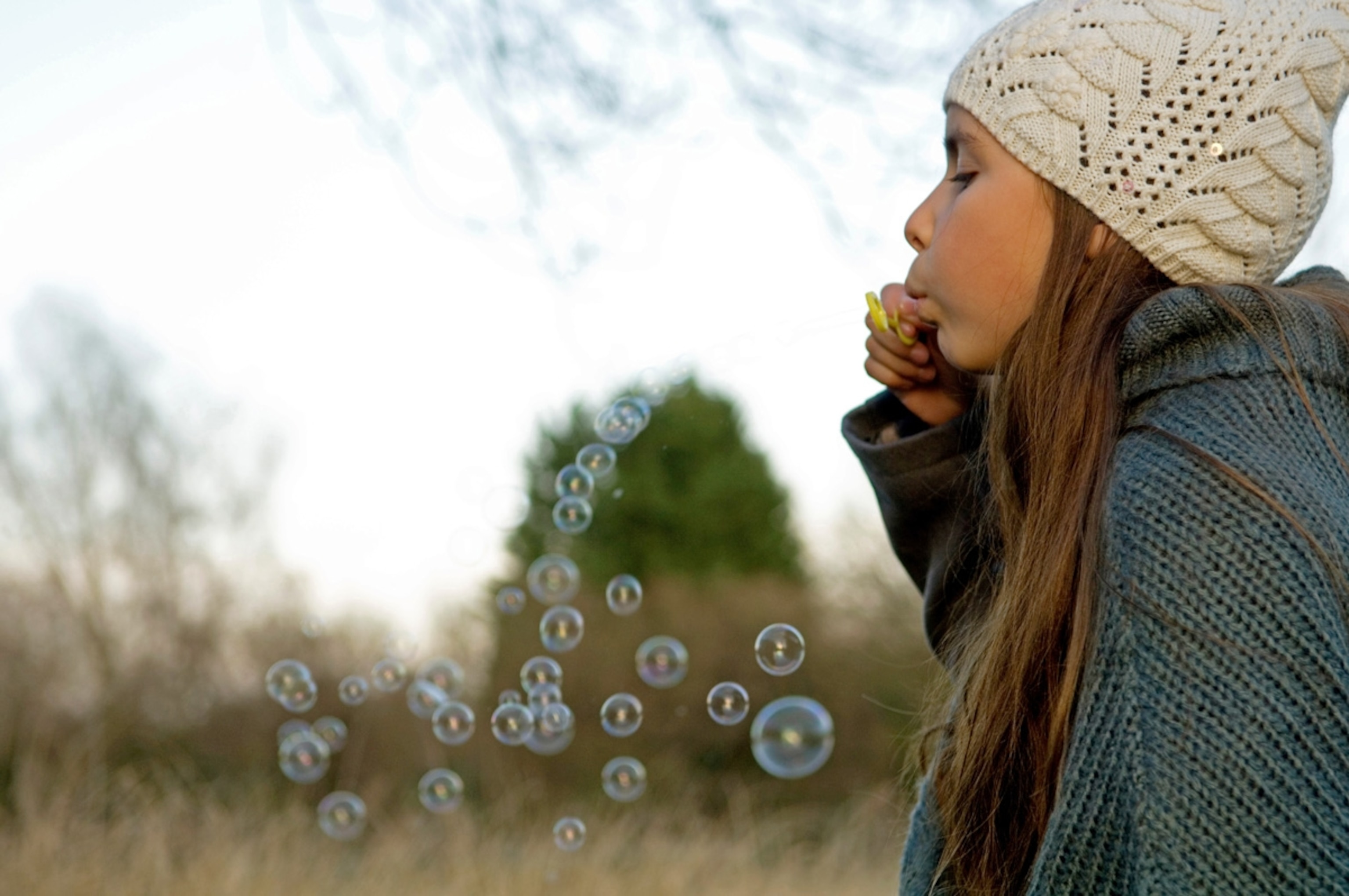 Side profile of a girl blowing bubbles with a bubble wand.