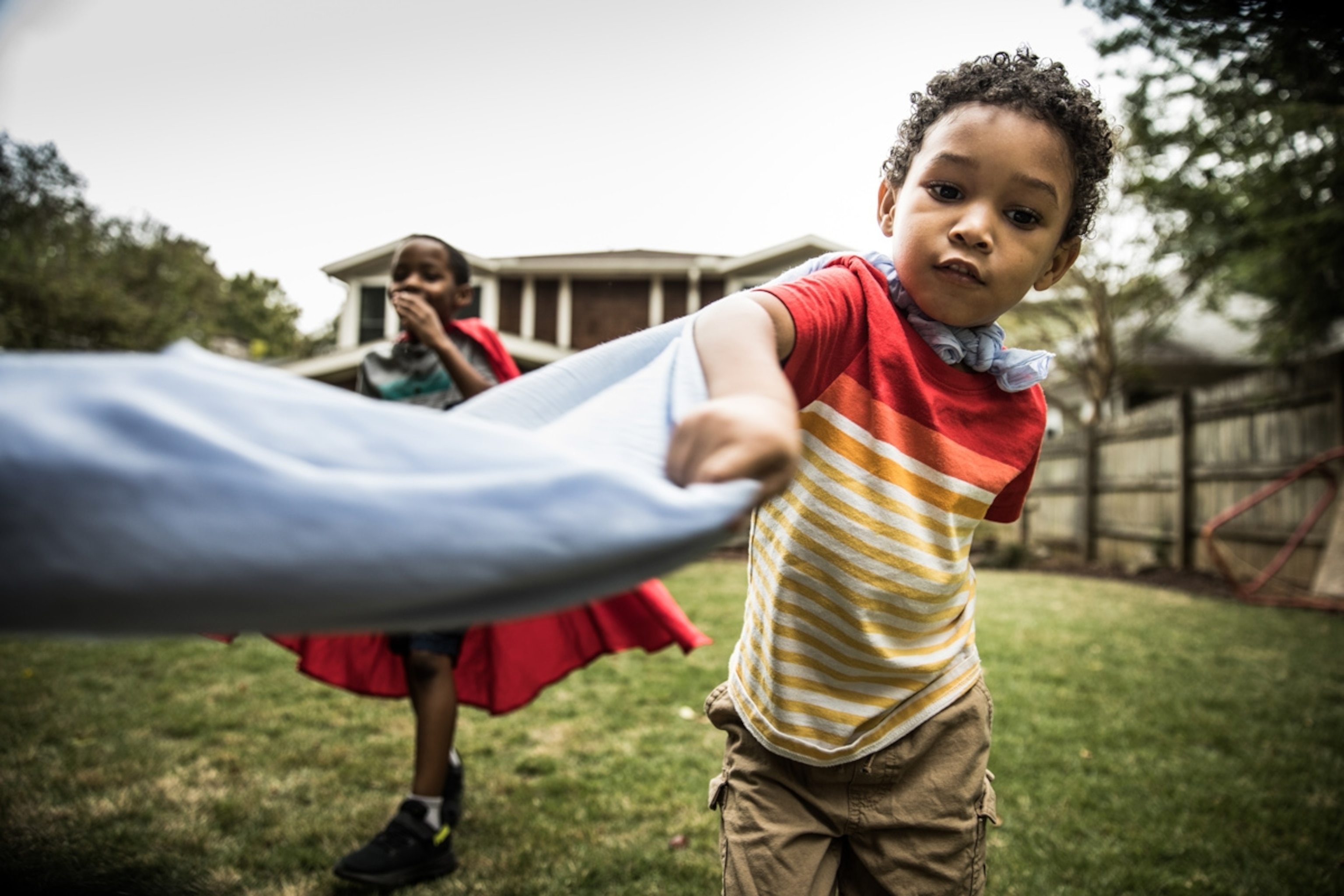Young boys (3 yrs and 6yrs) in capes playing in backyard.