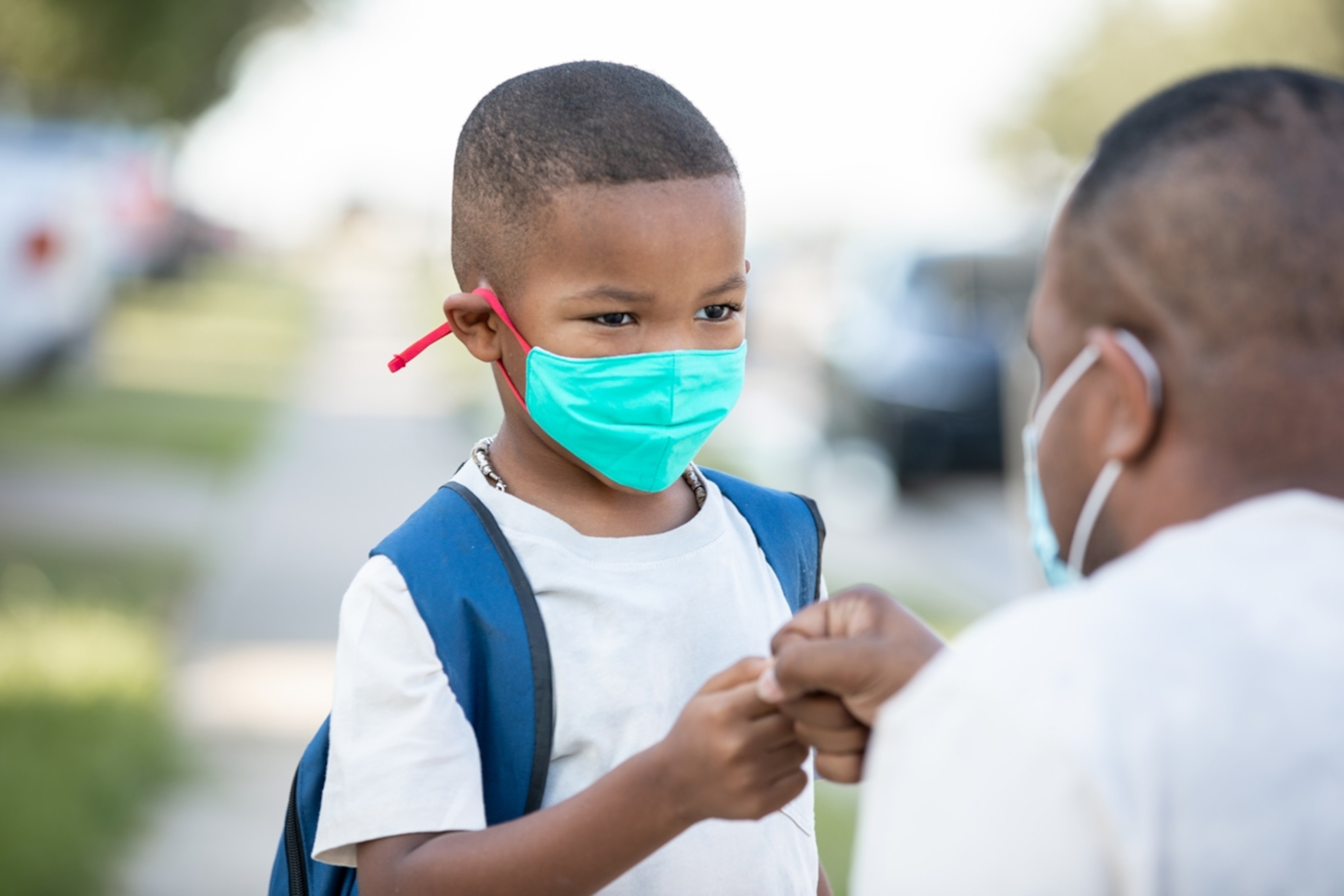 Father and son fist bump outside of school building on first day of kindergarten.