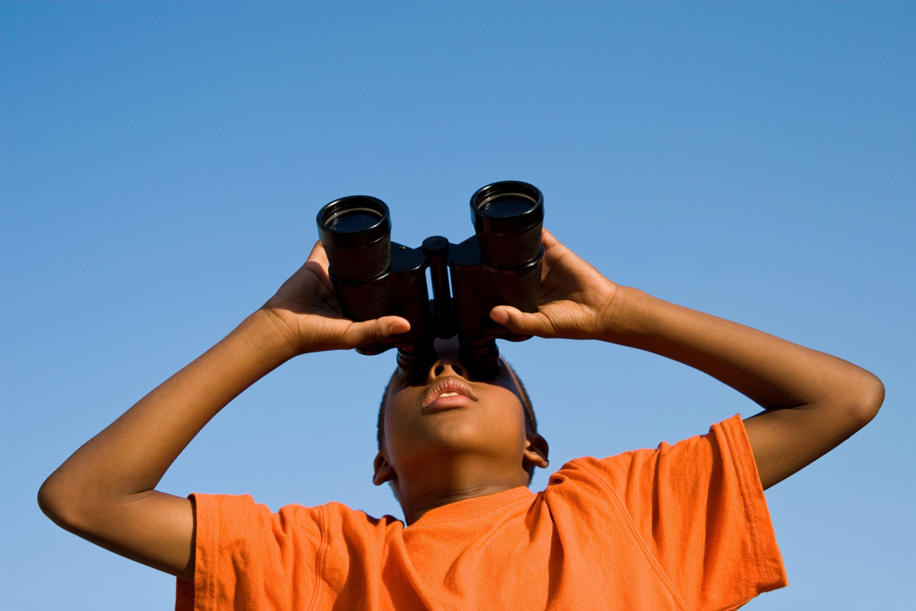 A boy looks skywards through binoculars.
