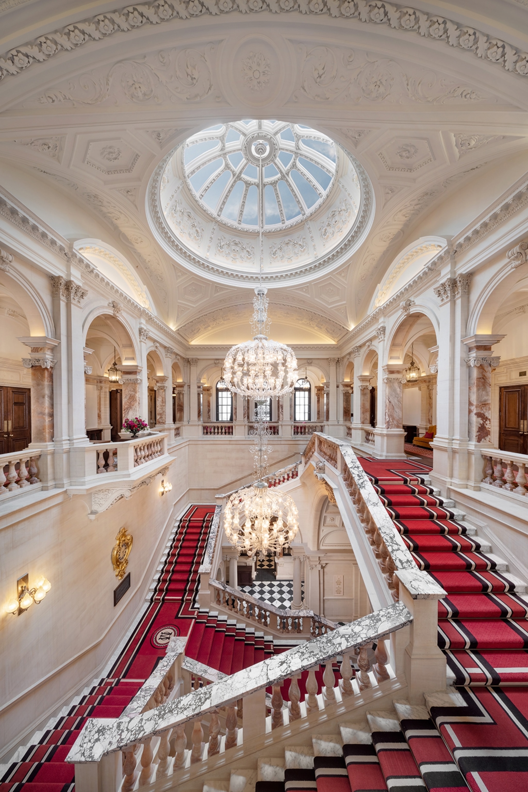 Grand stone and marble staircase with a chandelier and red, black and white carpet