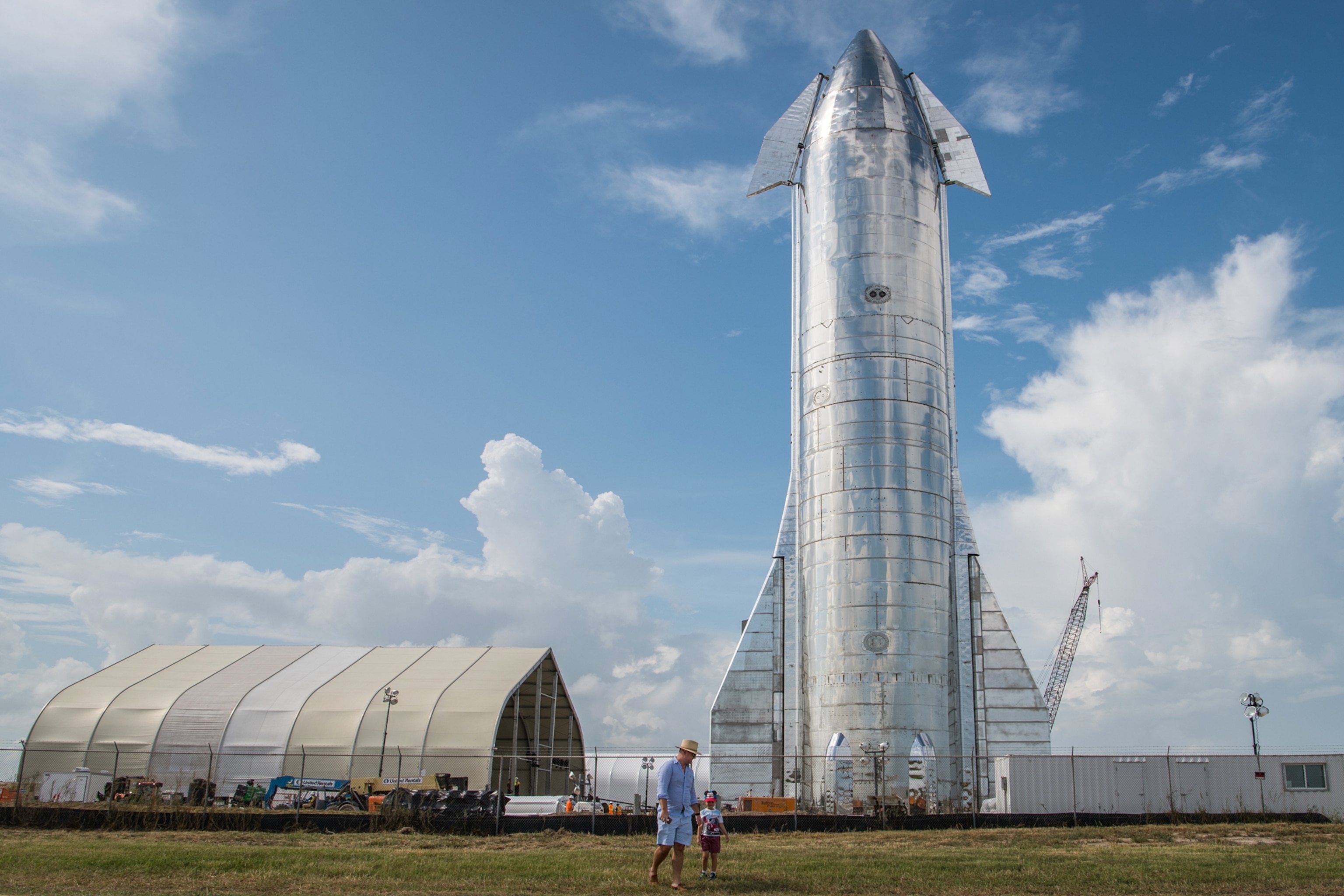silver rocket vertical on the ground under blue sky.