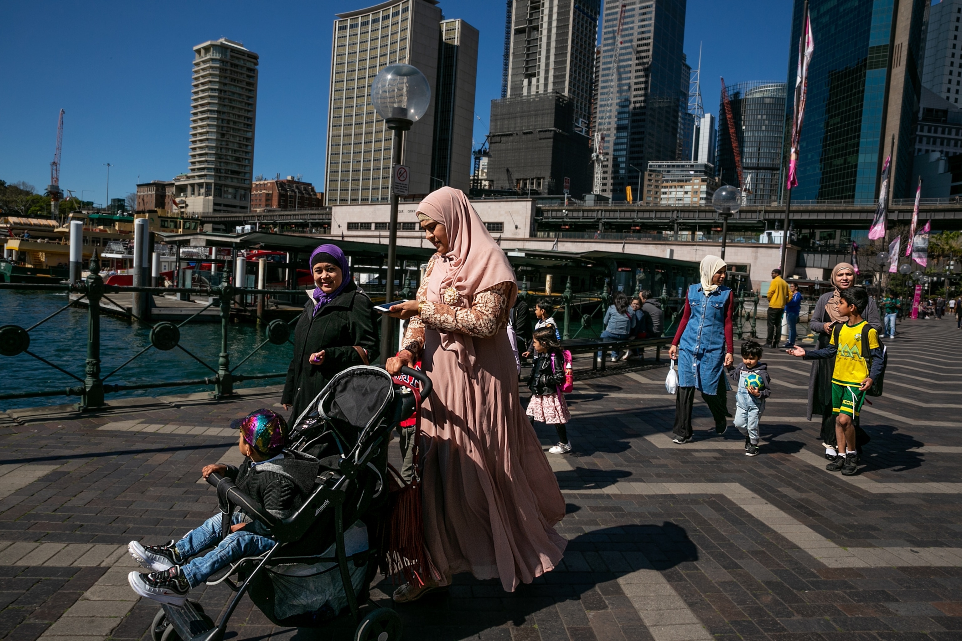 two woman walking along a harbor pushing a stroller
