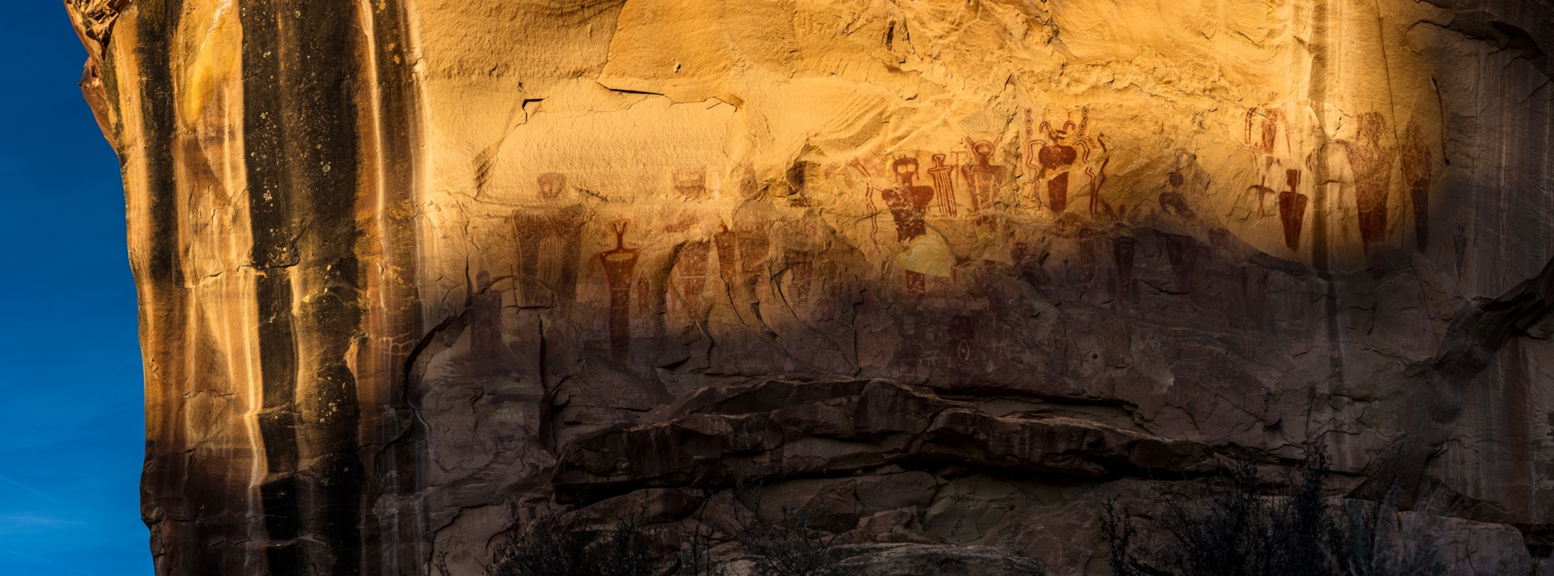 Panel of a mural with multiple figures undow low sunlight.
