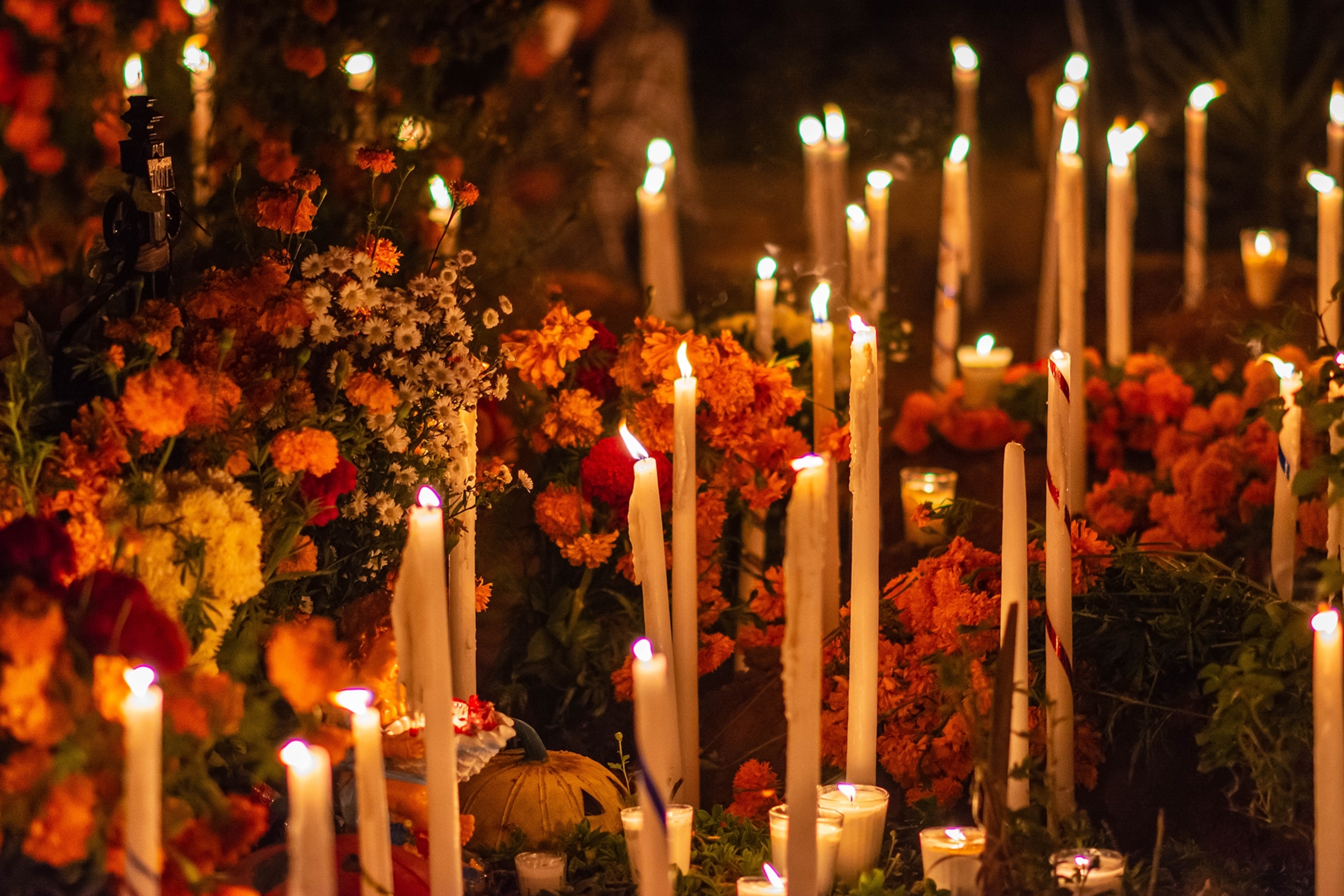 A close up of a sea of lit candles in between flowers on an altar.