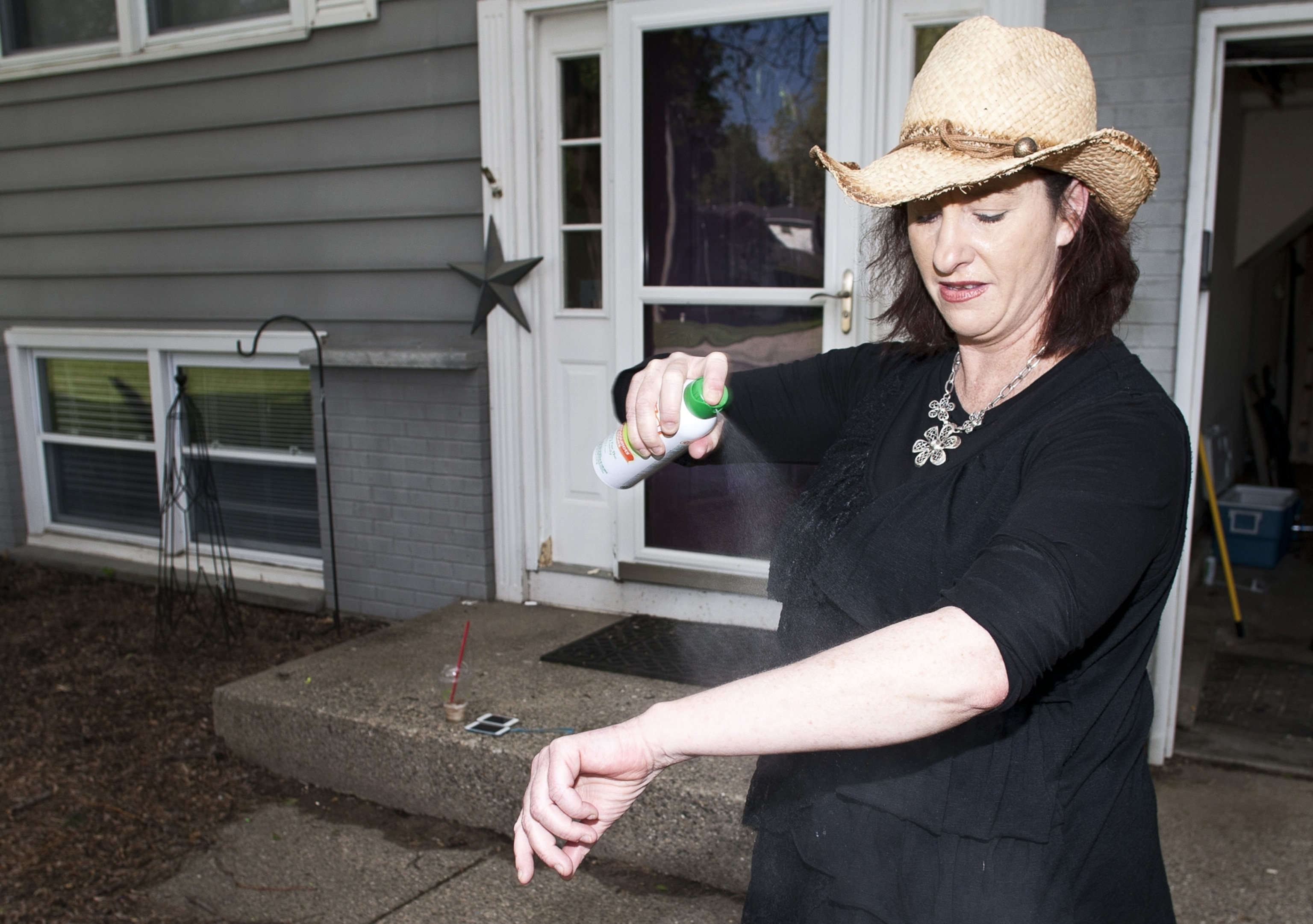 A woman with a hat rolled up sleeve sprays, bug spray on her body.