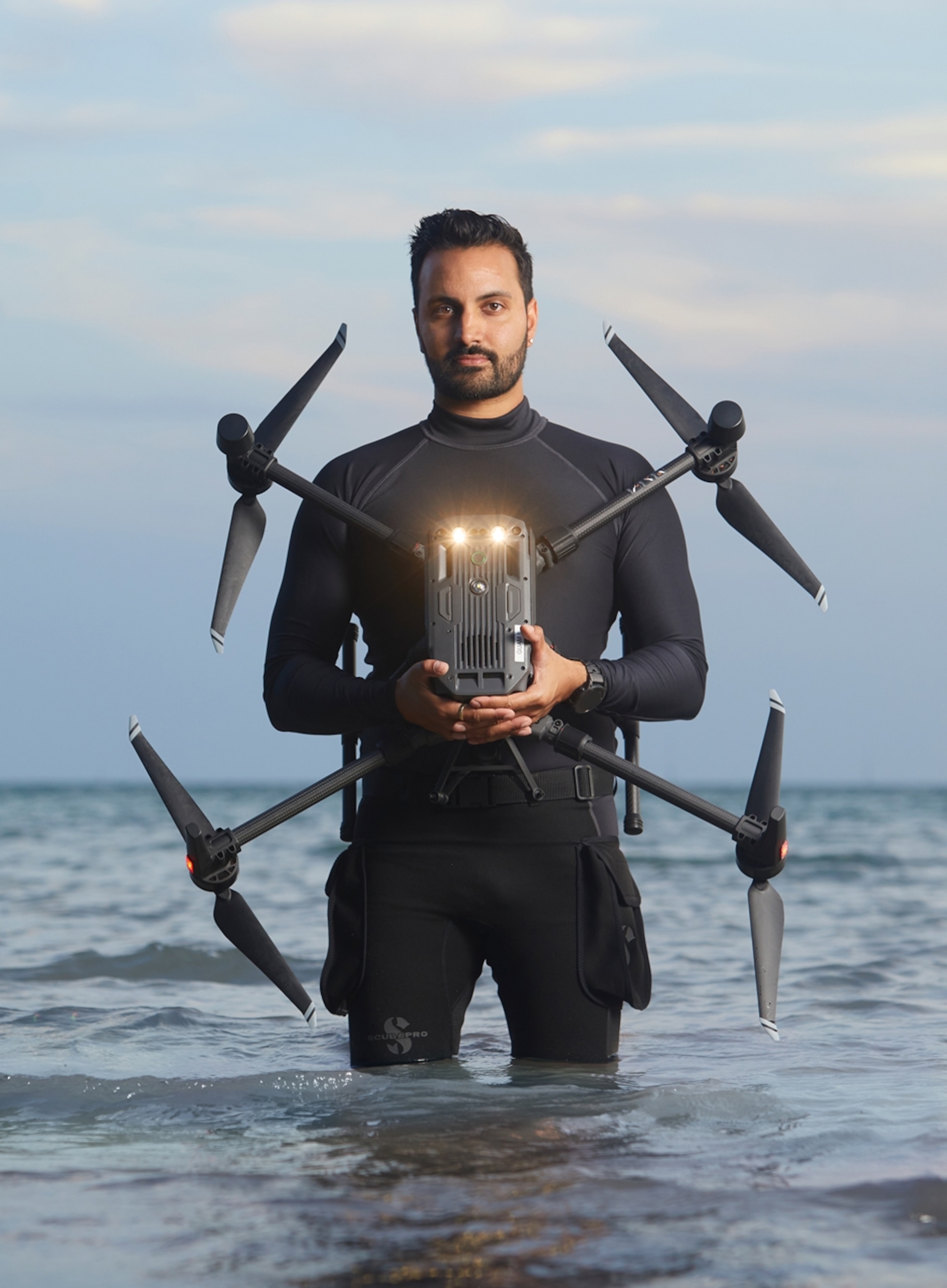 Picture of man in wet suite standing in water with drone in his hands.