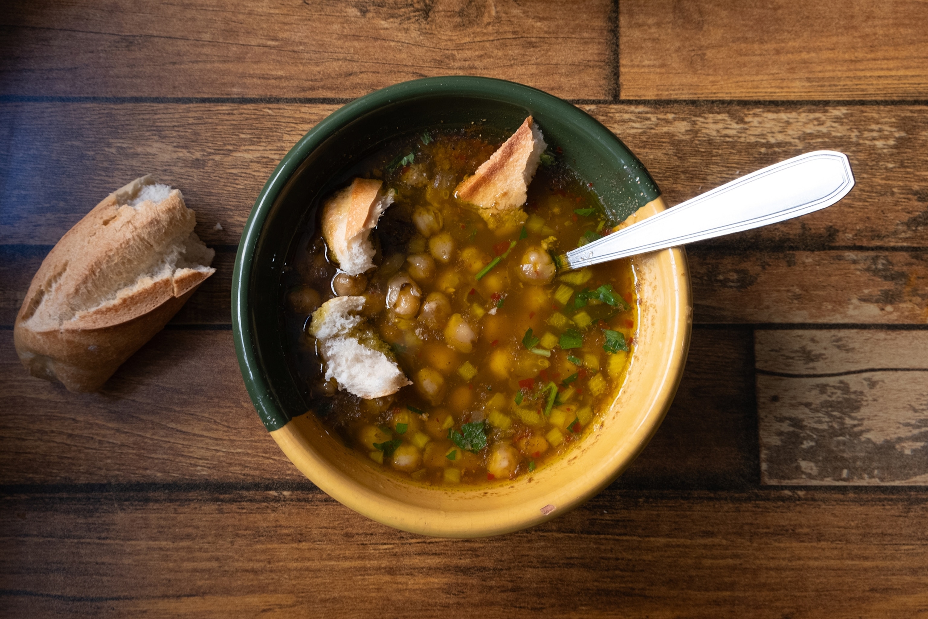 A bowl of clear chickpea soup with herbs and chunks of white bread.