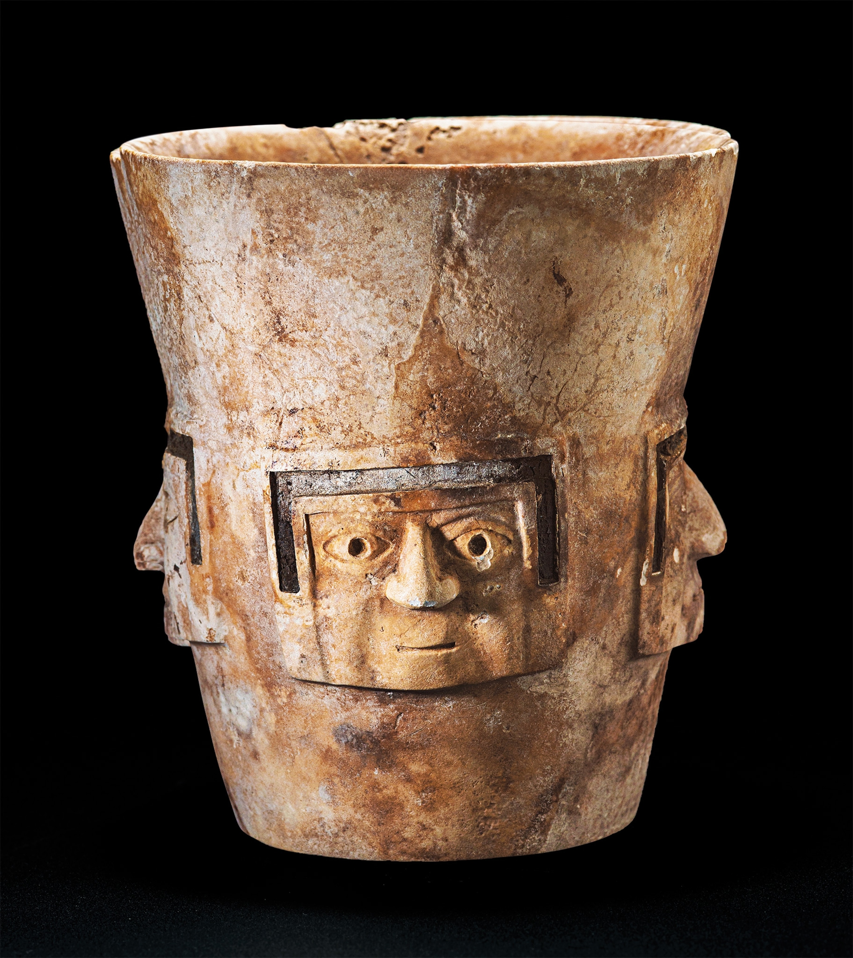 Working with an alabaster-like Andean stone, an artisan carved this drinking cup adorned with human faces.