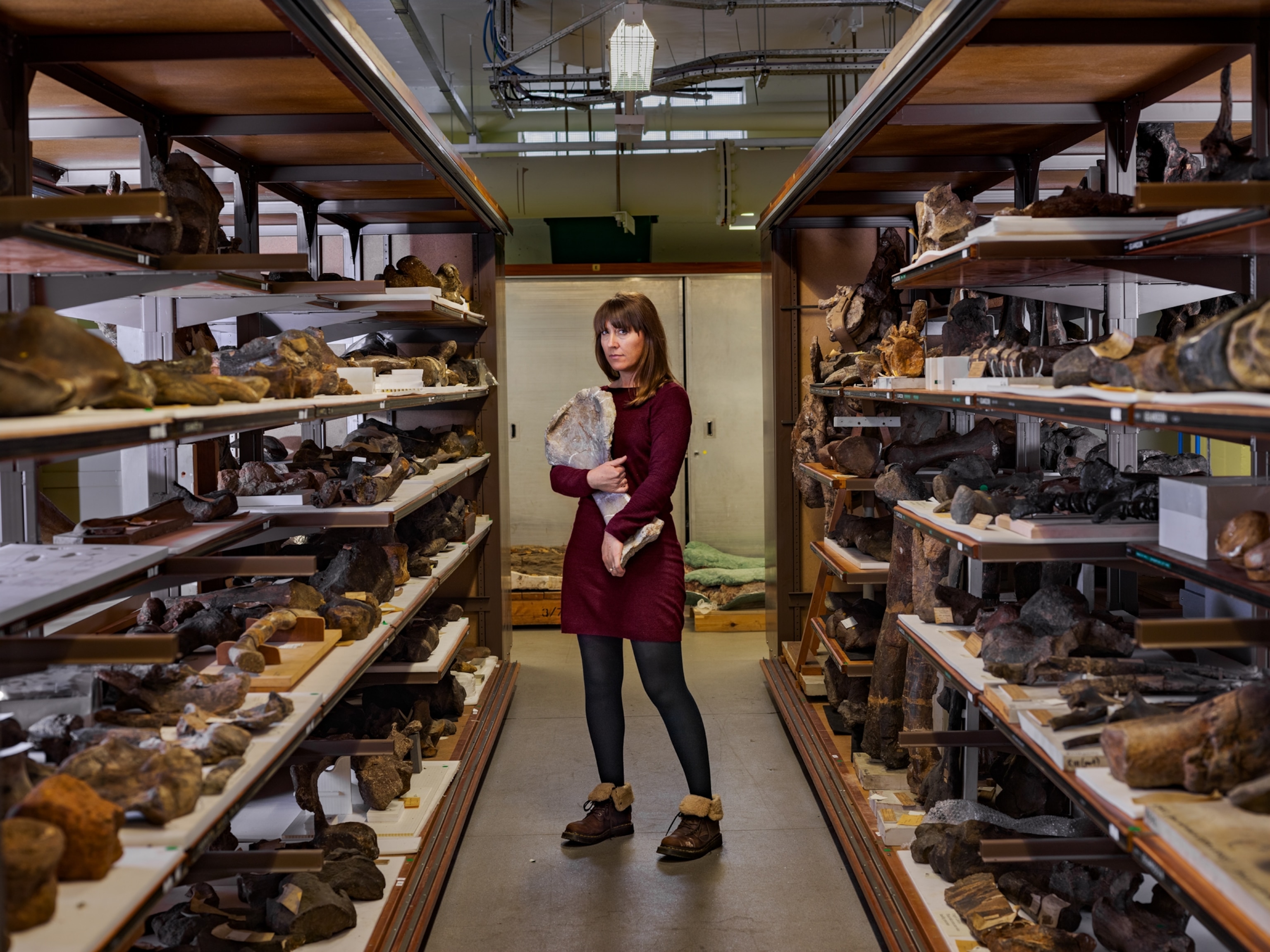 a woman standing in the aisle of a fossil collections room