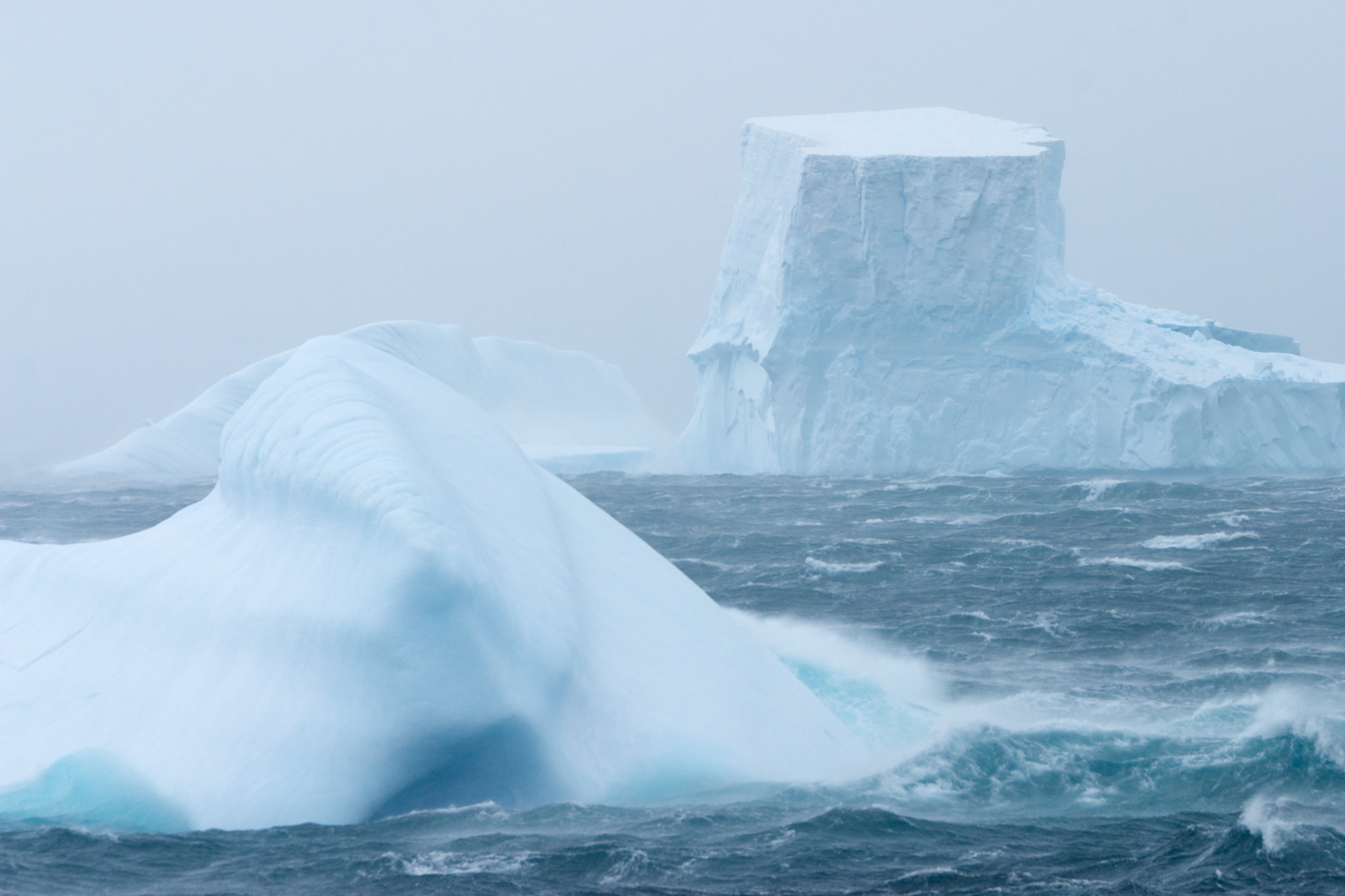 Spindrift blows off icebergs and waves in gale winds over stormy sea in Drake Passage, Southern Ocean, Antarctica.