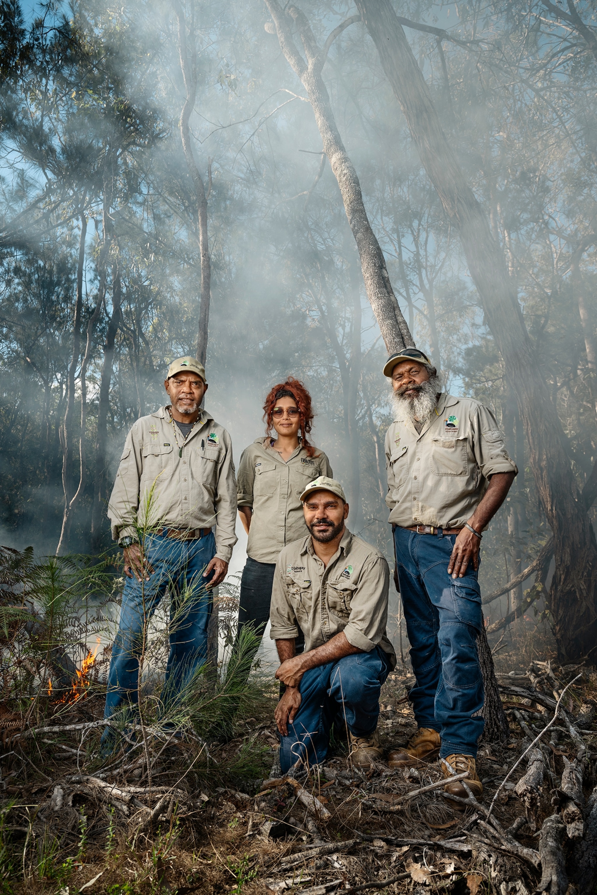 Four rangers in jeans and button downs pose in a forest with smoke behind them