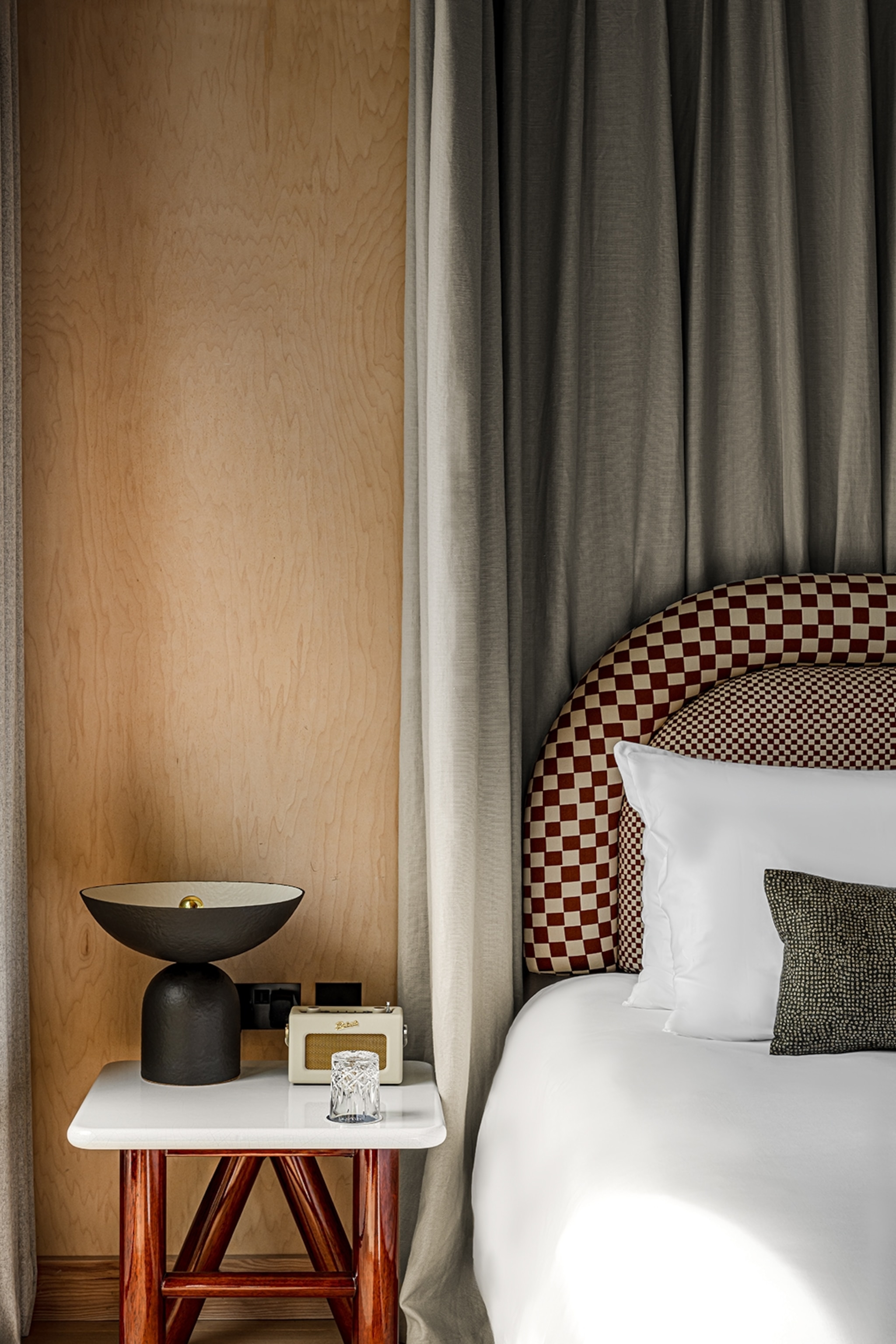 A focused shot on the sleek bedside area of a hotel room with a chequerboard headboard and retro radio.