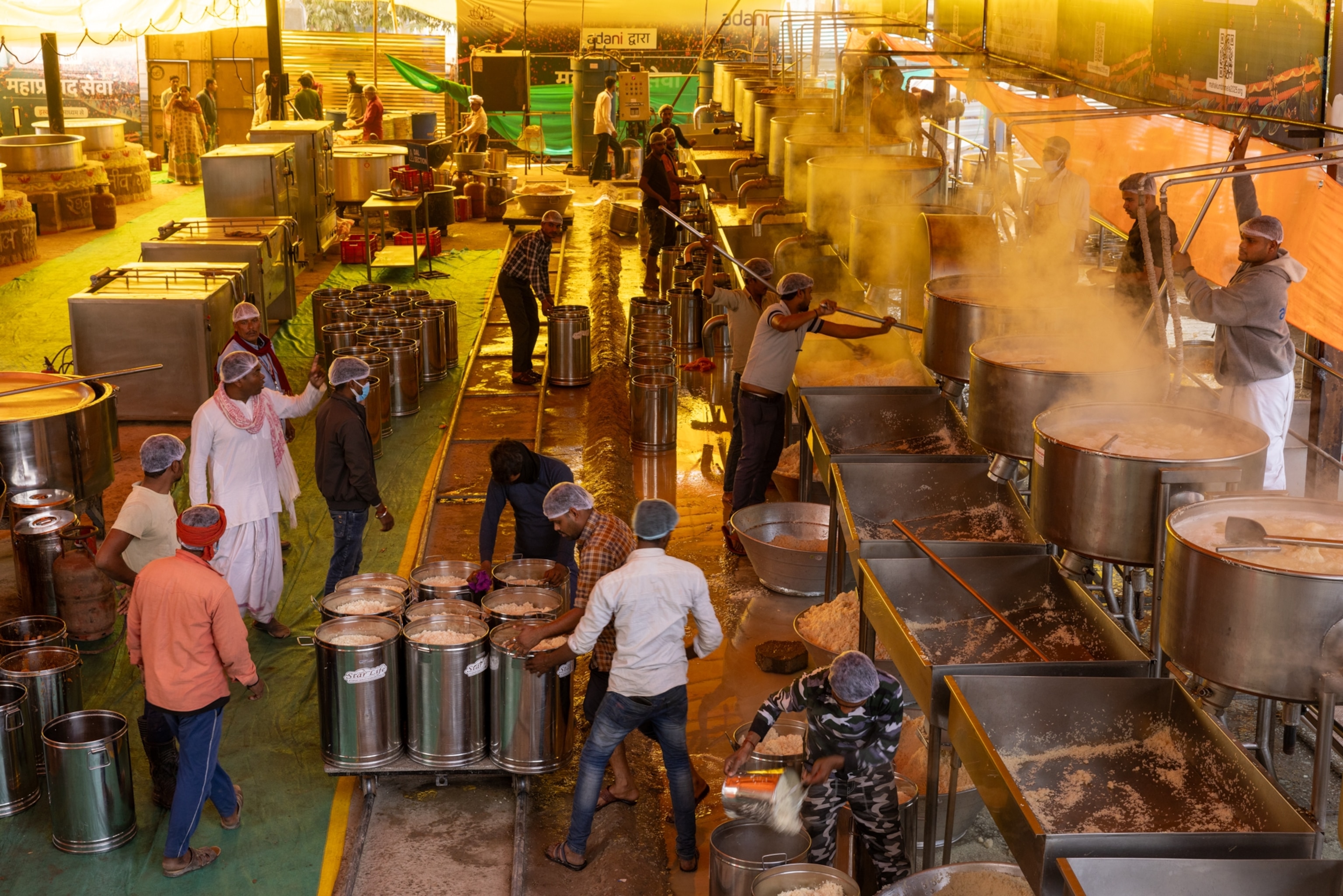 A large group of men do various tasks to cook a massive quantity of meals.