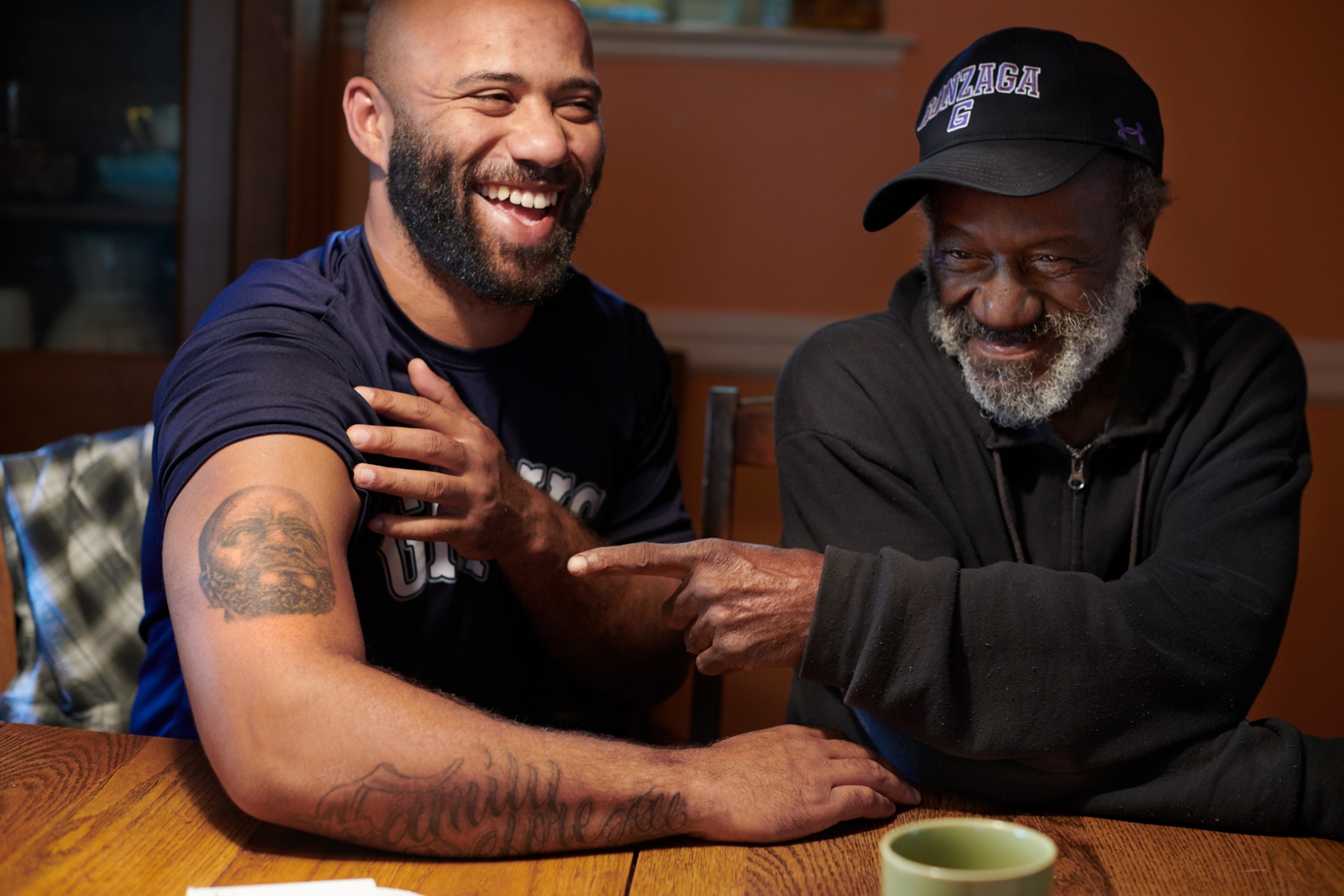 old man in black baseball hat and younger man with tattoo on his arm.