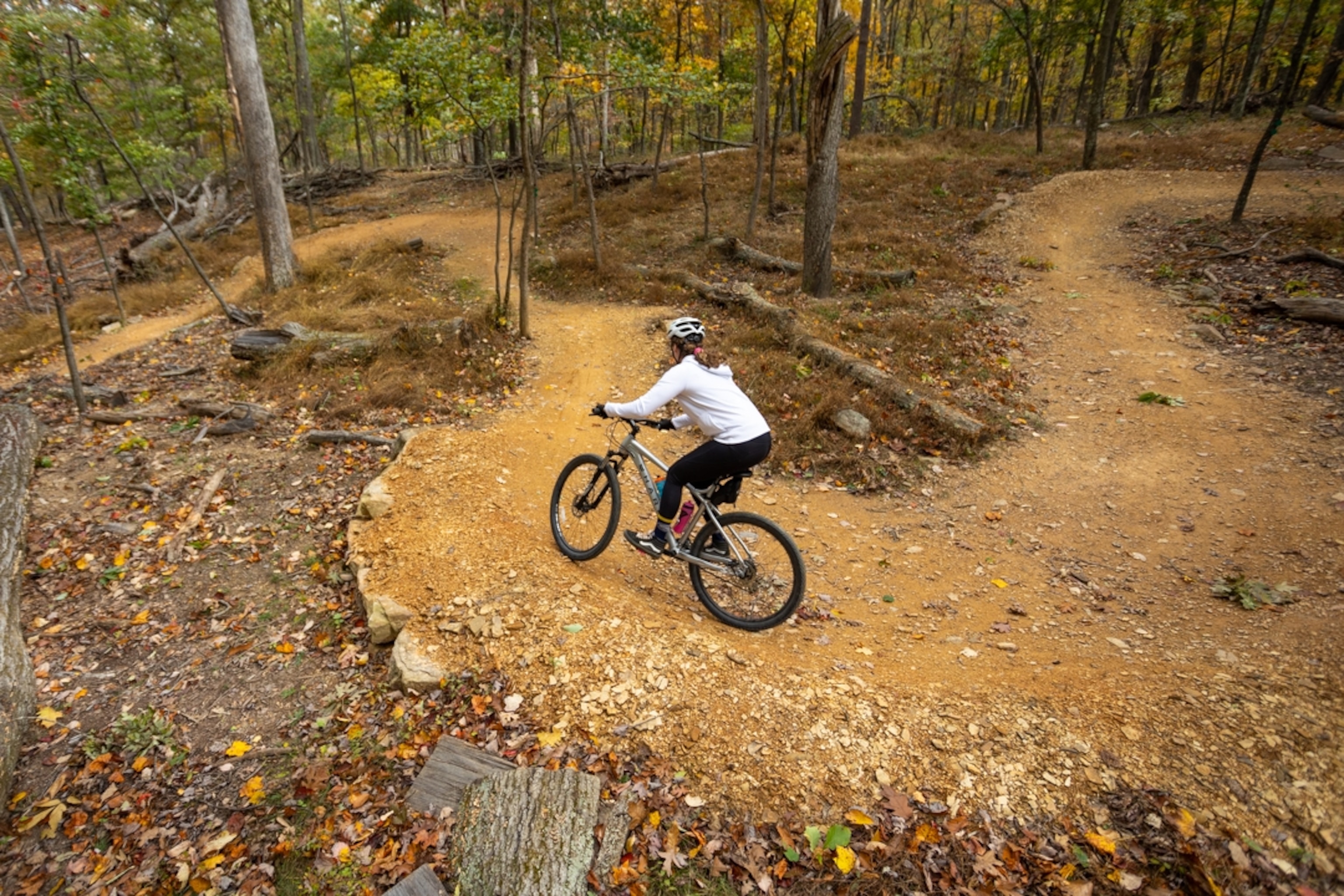A cyclist rides her bike around a curve in a bike trail carved out of a forest in Cacapon State Park