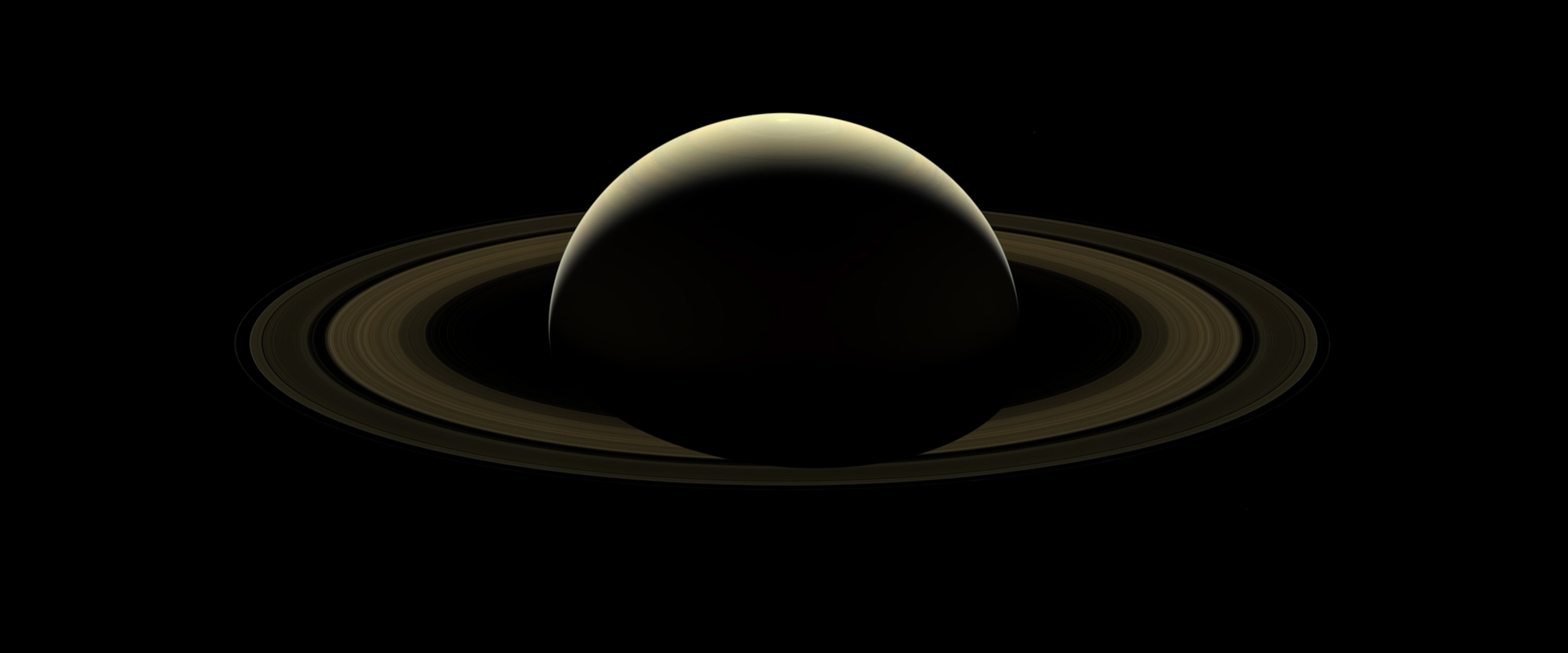 A crescent of the top of Saturn surrounded by its golden rings in pale light.