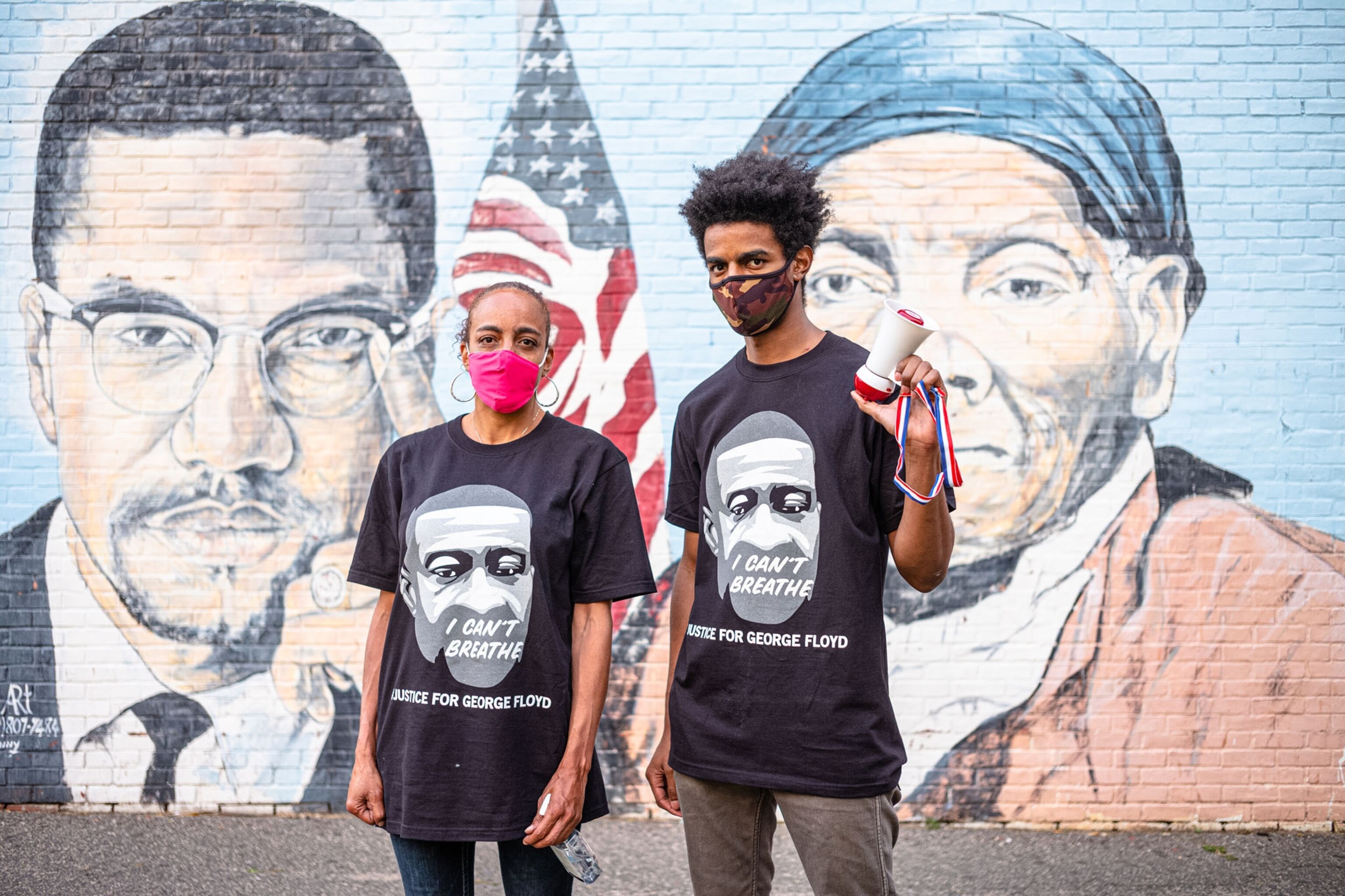 masked woman and man in t-shirts with portrait against mural on background.