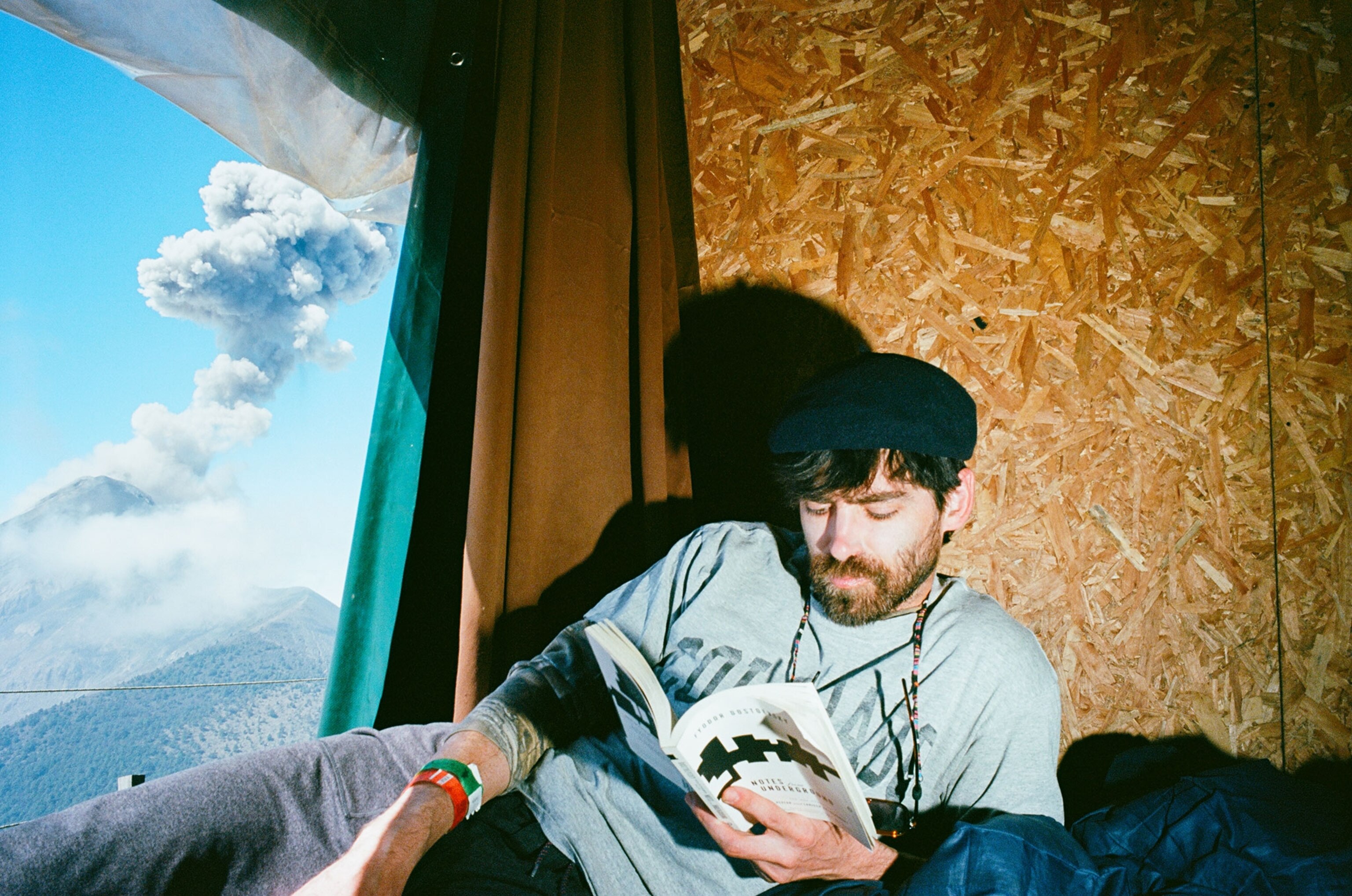 Hiker Charlie Ballinger reads in his cabin at base camp on Volcán de Acatenango while Volcán de Fuego erupts in the distance.