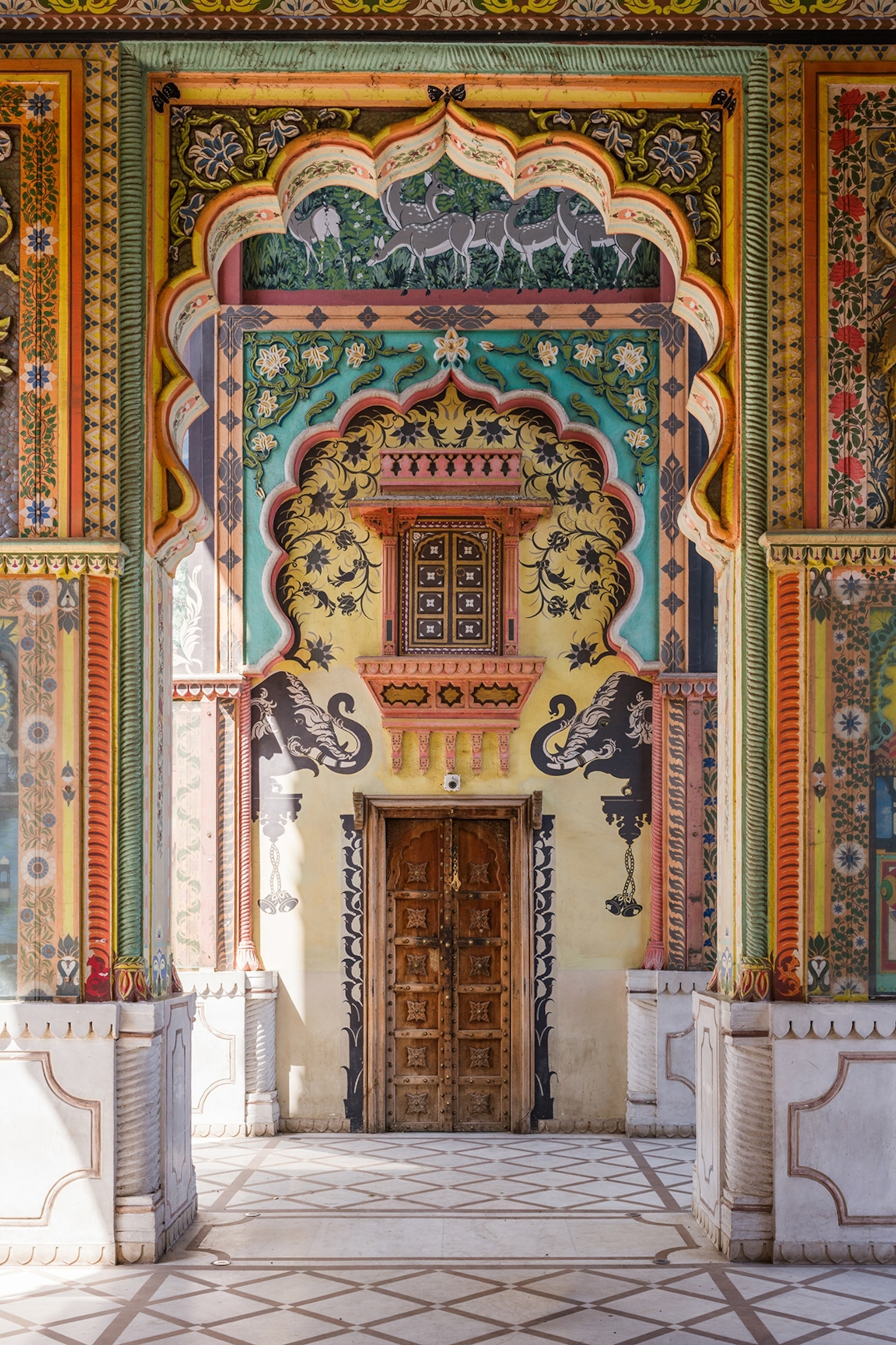 A focused look down a multi-layered and ornately decorated, colourful gate with a door at its centre and wall illustrations of elephants.