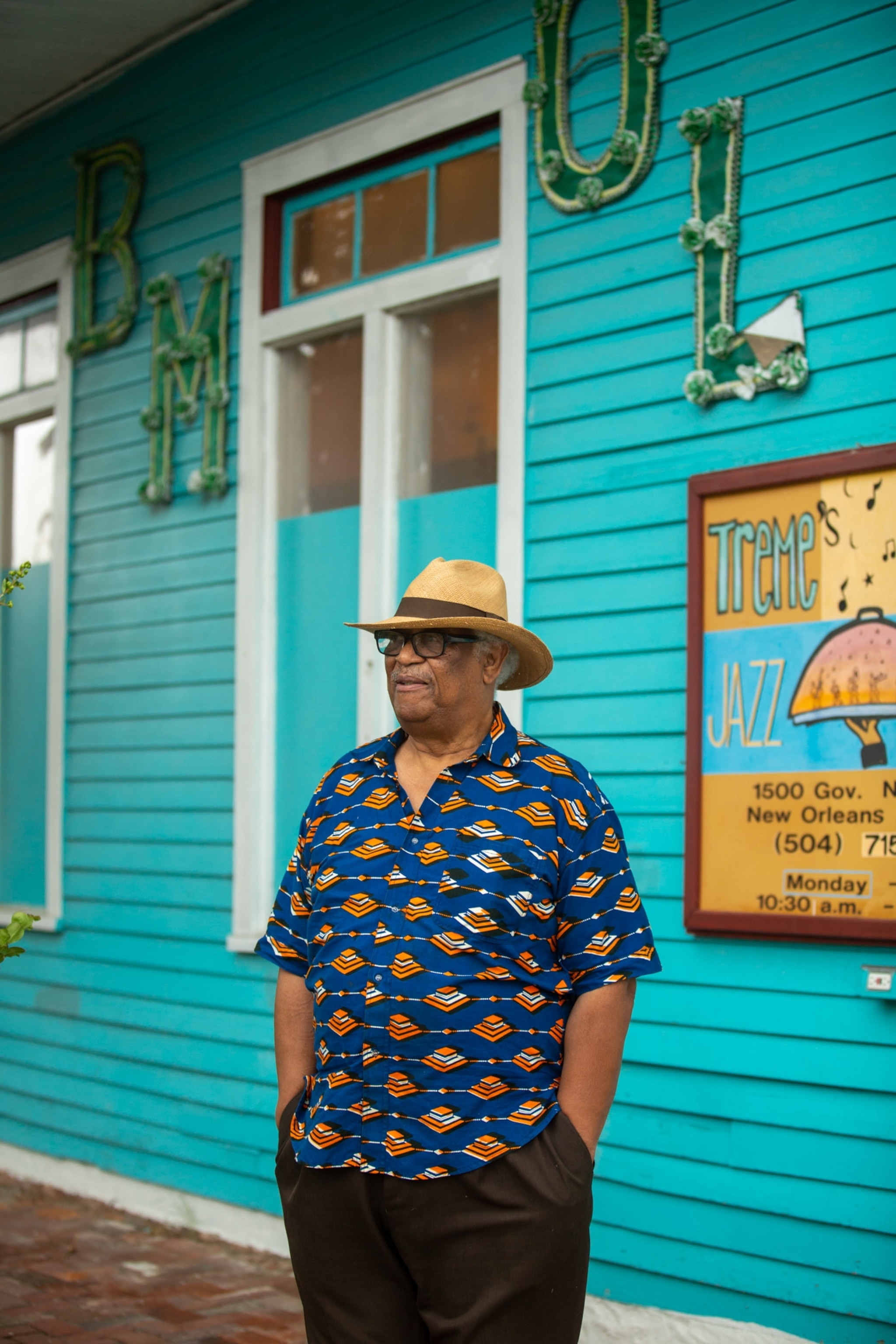 a man in a brimmed straw hat standing outside of a teal building
