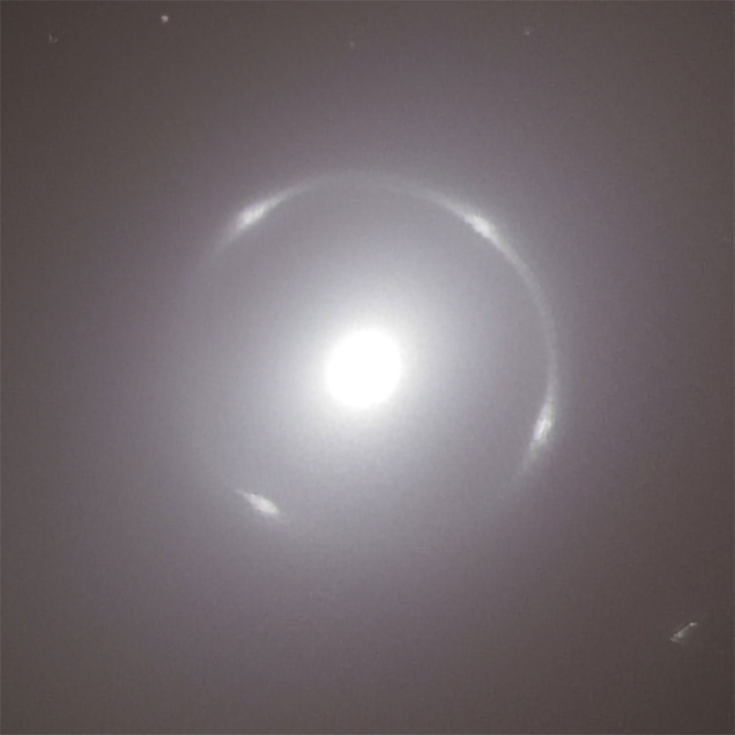A thin ring of a perfect circular shape and a piercingly bright white disc in its middle are the protagonists of this image. They stand out against a uniformly coloured background of a hazy dark grey. The ring appears as if it was a faint brush stroke, where at four evenly spaced spots more pressure was applied on the brush. These stand out in the ring as four brighter and thicker spots. The white disc within the ring gives the impression of a gaping hole in the image, through its stark contrast to the dark background