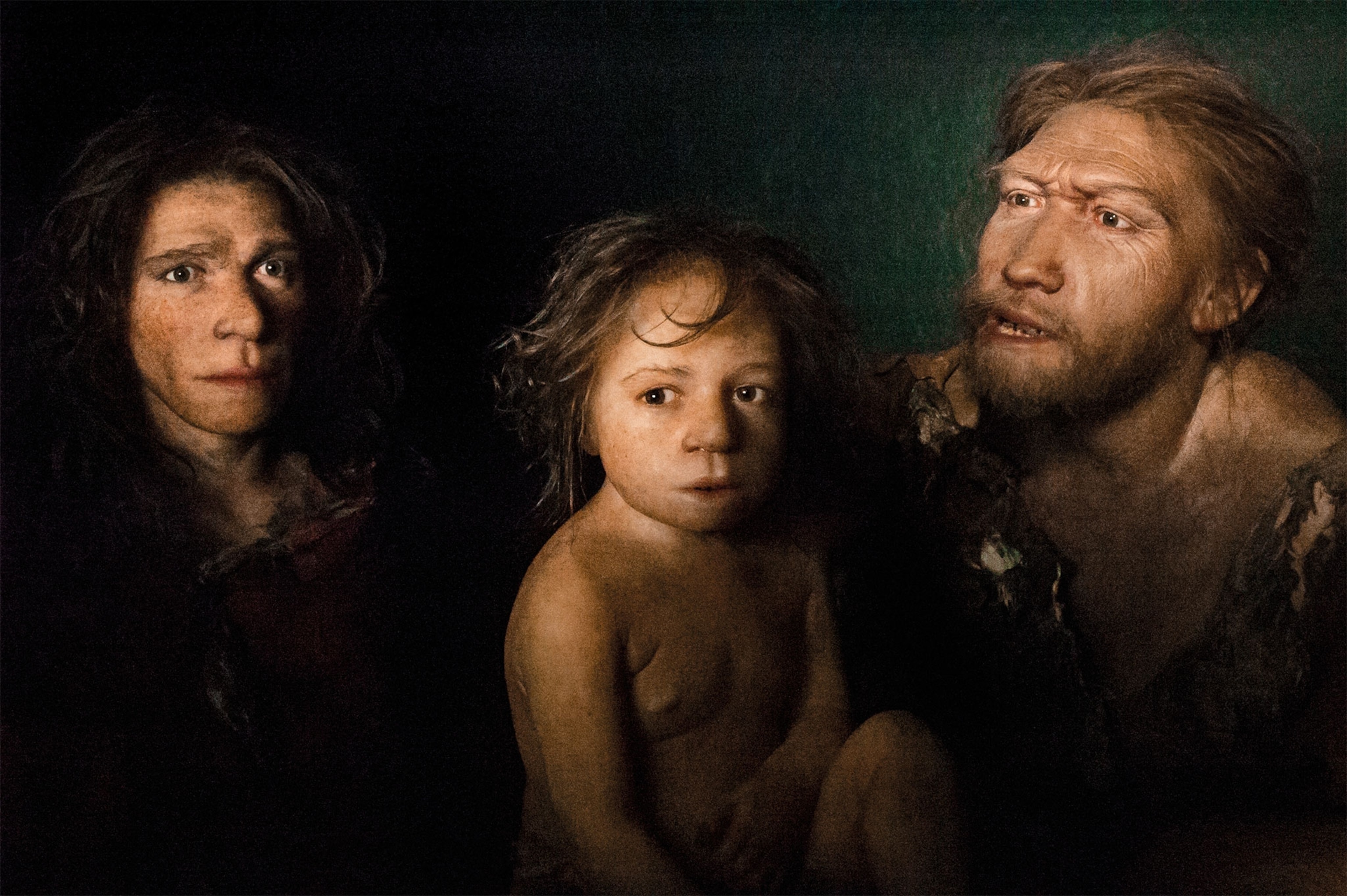 3 recontructions of Neanderthals in a line against a black background
