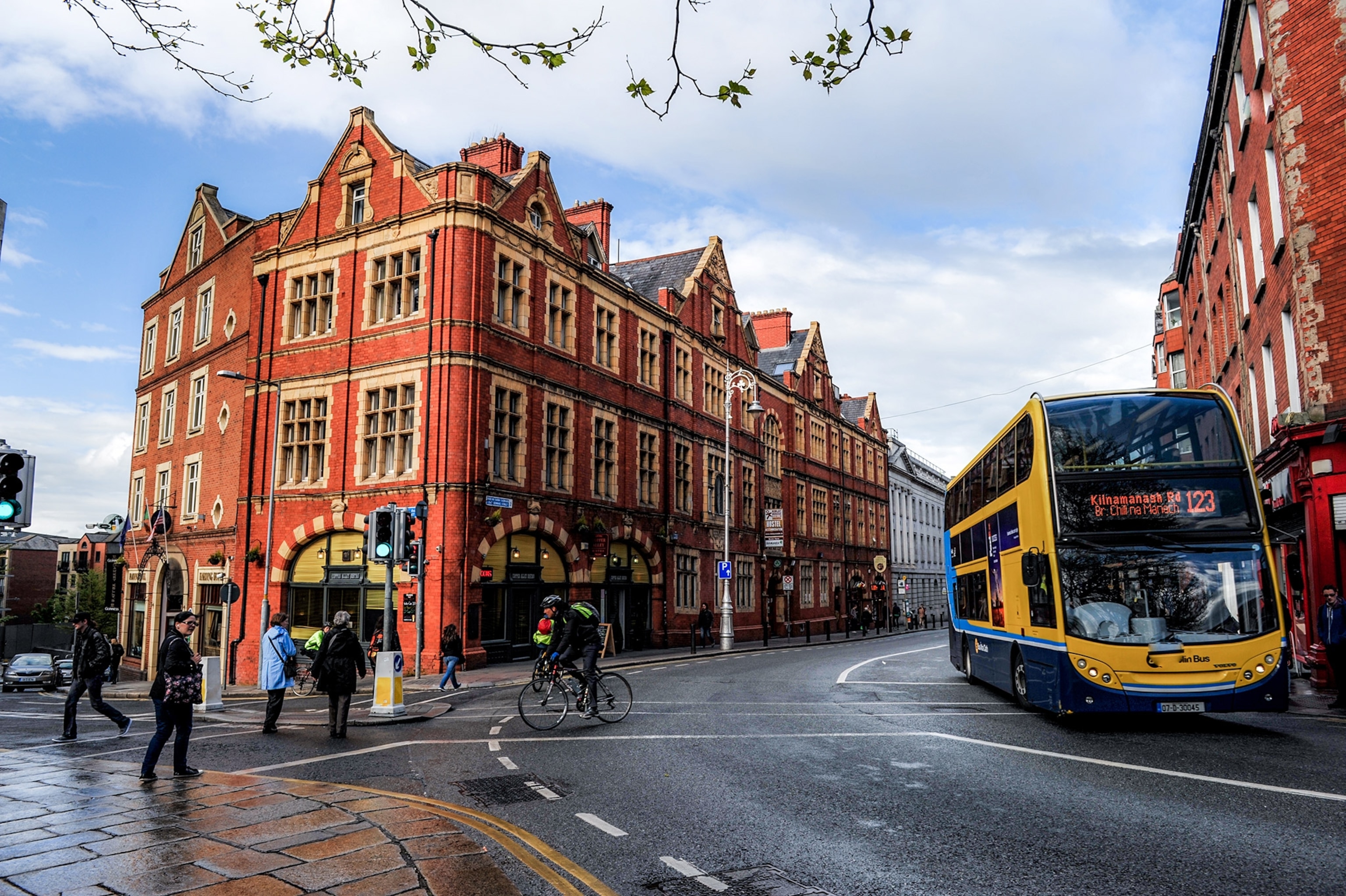Red brick buildings line the roads while a bus turns and people cross the street.