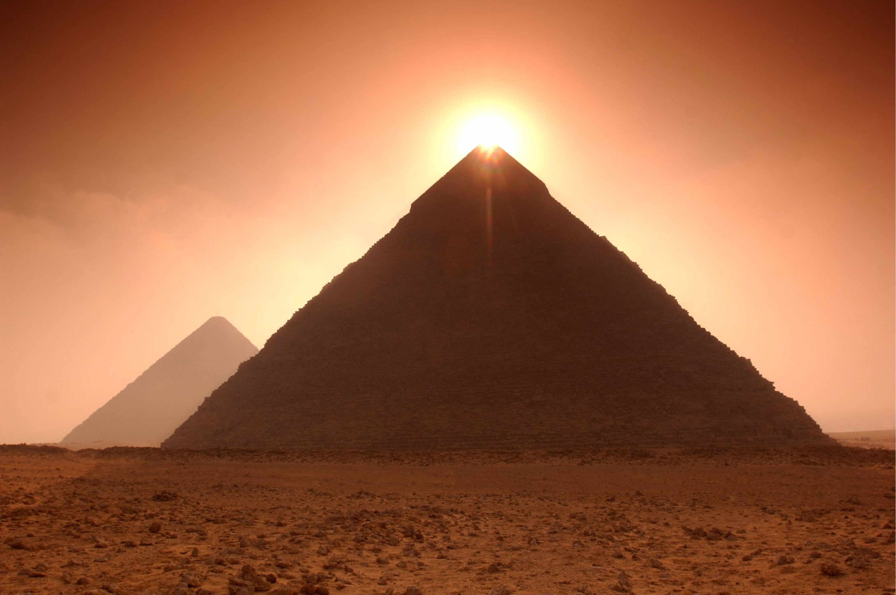 The brightly shining just above the peak of an Egyptian pyramid beneath a dusty red sky