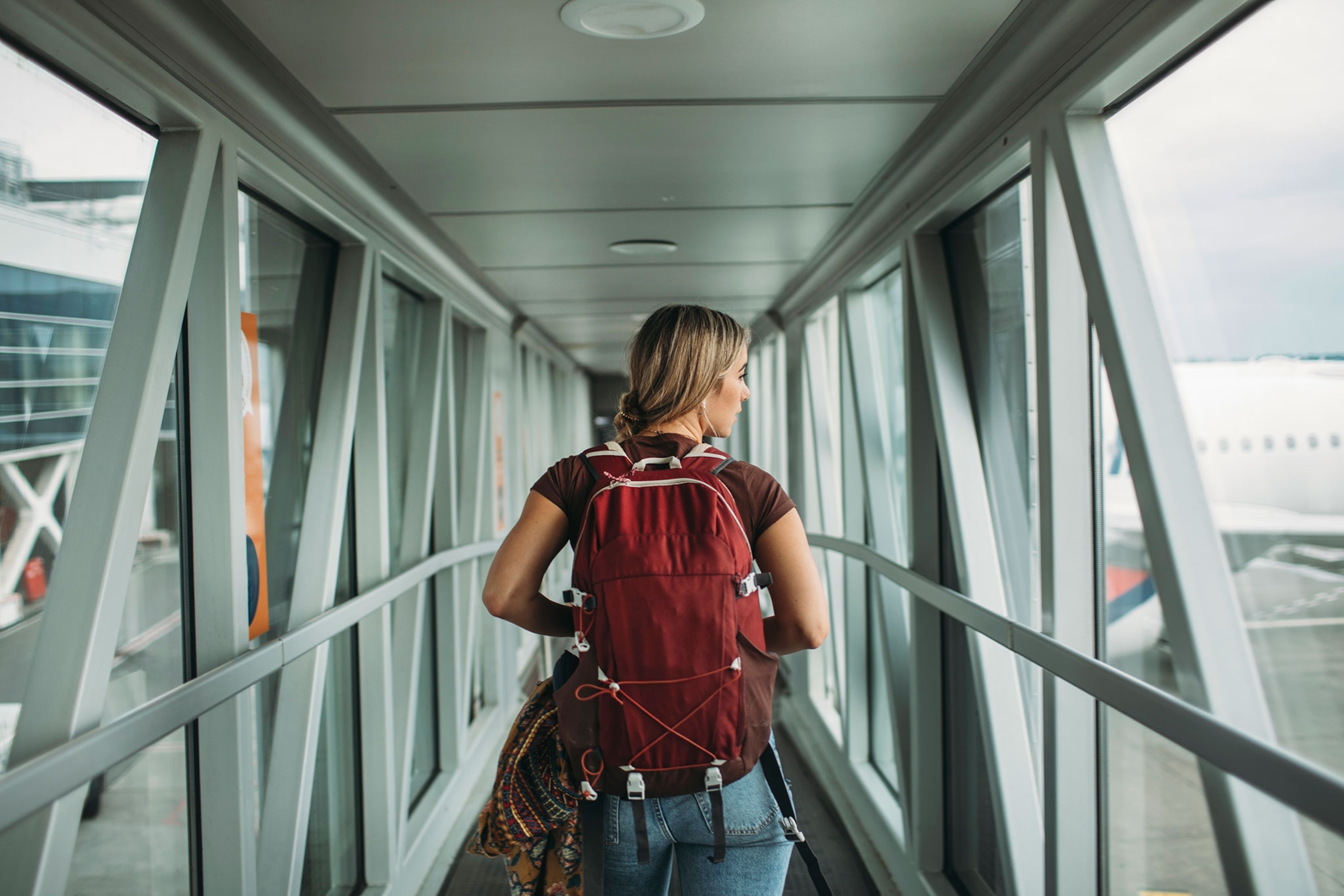 A person wearing a red backpack walking down a hallway to a plane.