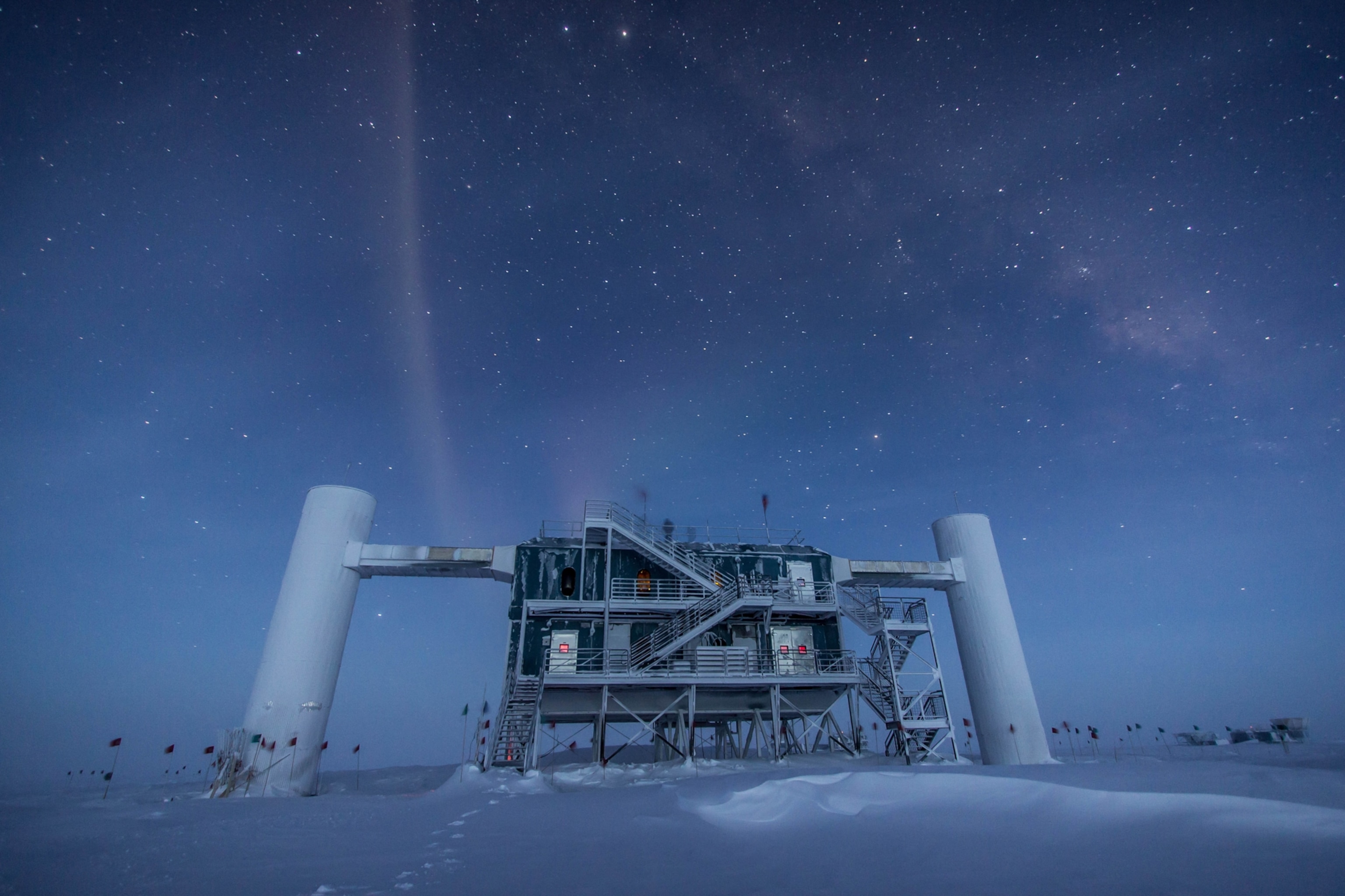 The IceCube Neutrino Observatory in Antarctica with the Milky Way visible in the night sky above.