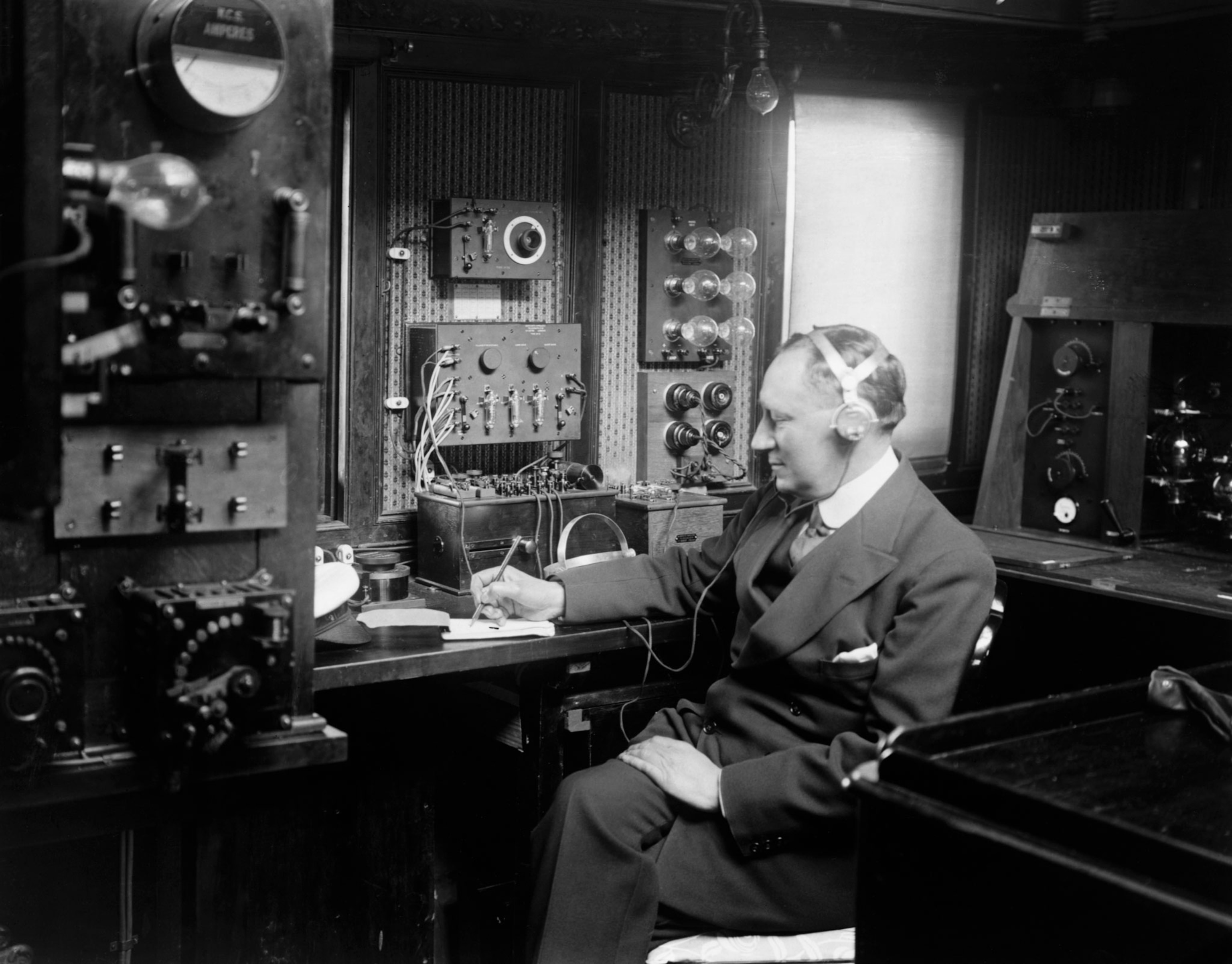 a man writing surrounded by a machine with many dials and cords