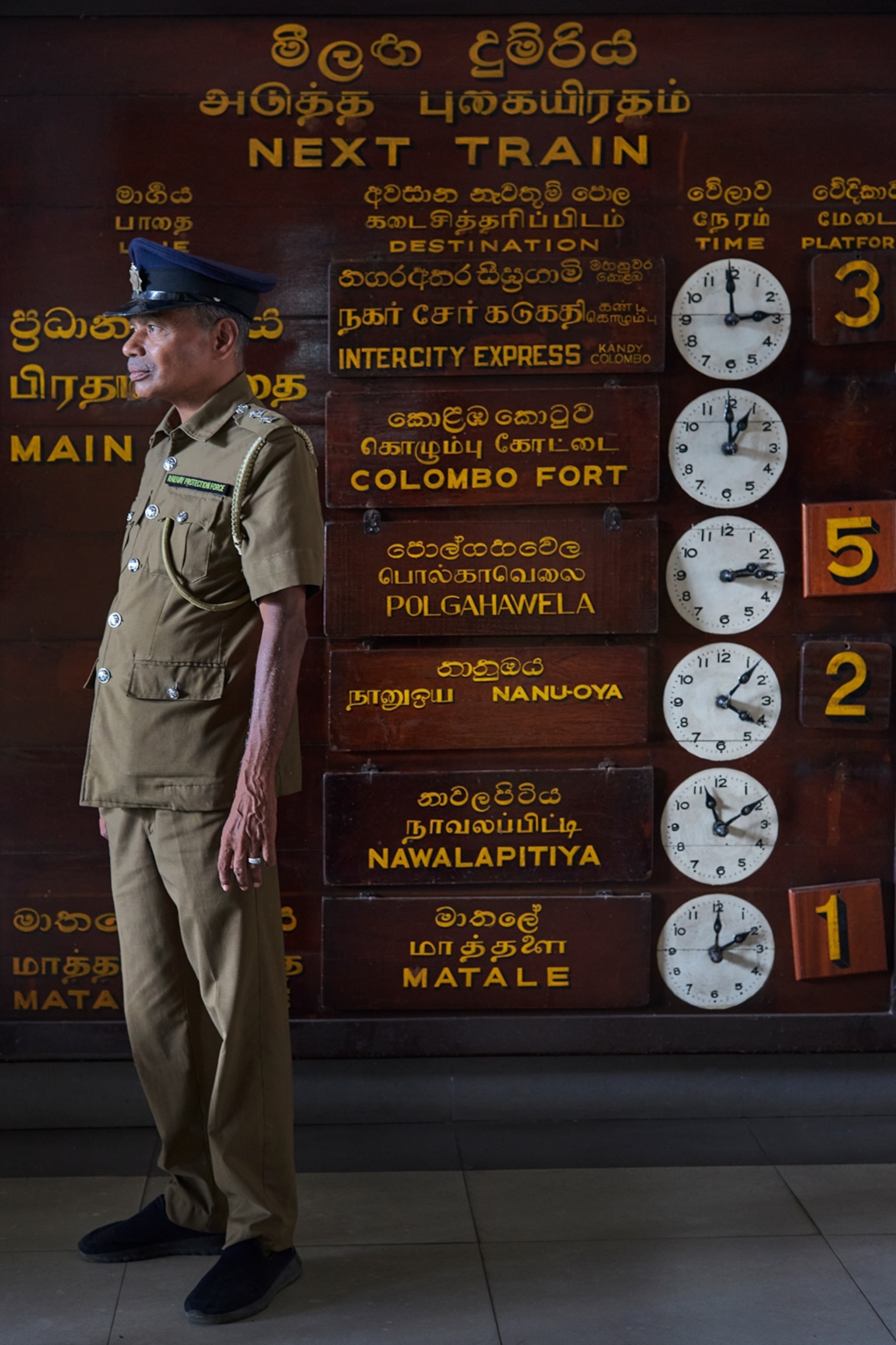 A railway police officer standing in front of a wall with clocks showing different timezones.