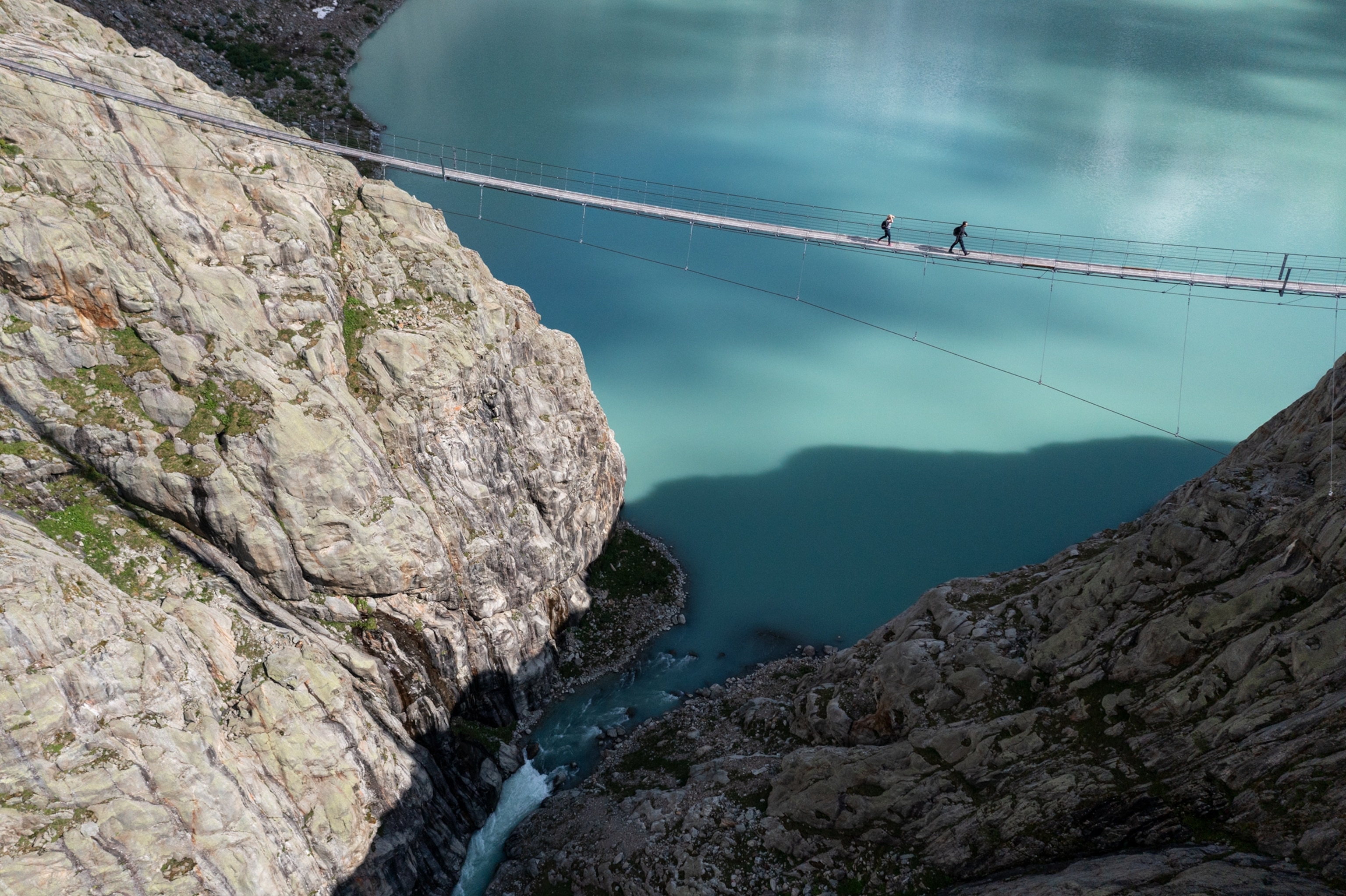 Picture of people walking on a suspension bridge over blue water.