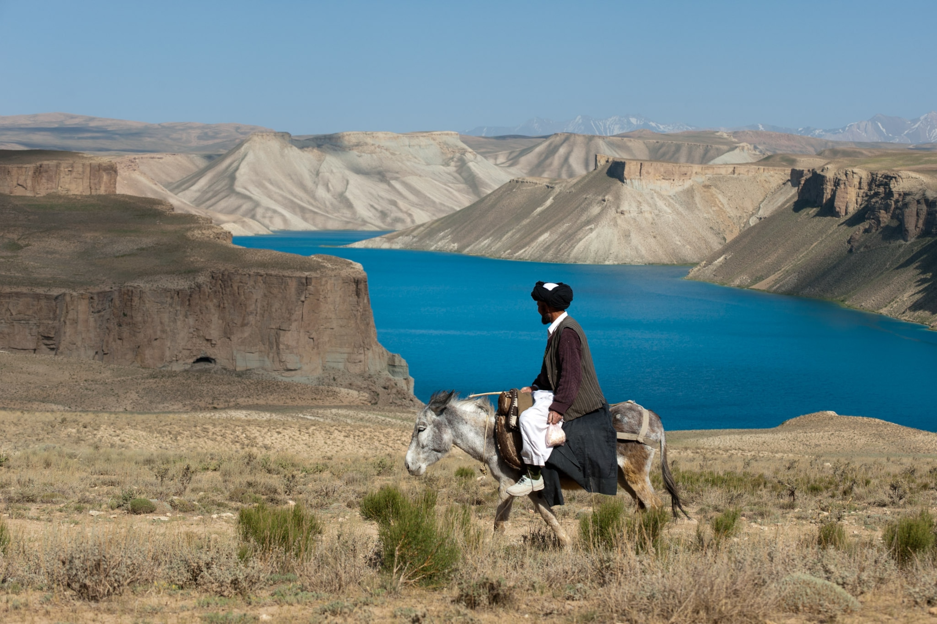 A man on a donkey looks at a blue lake.