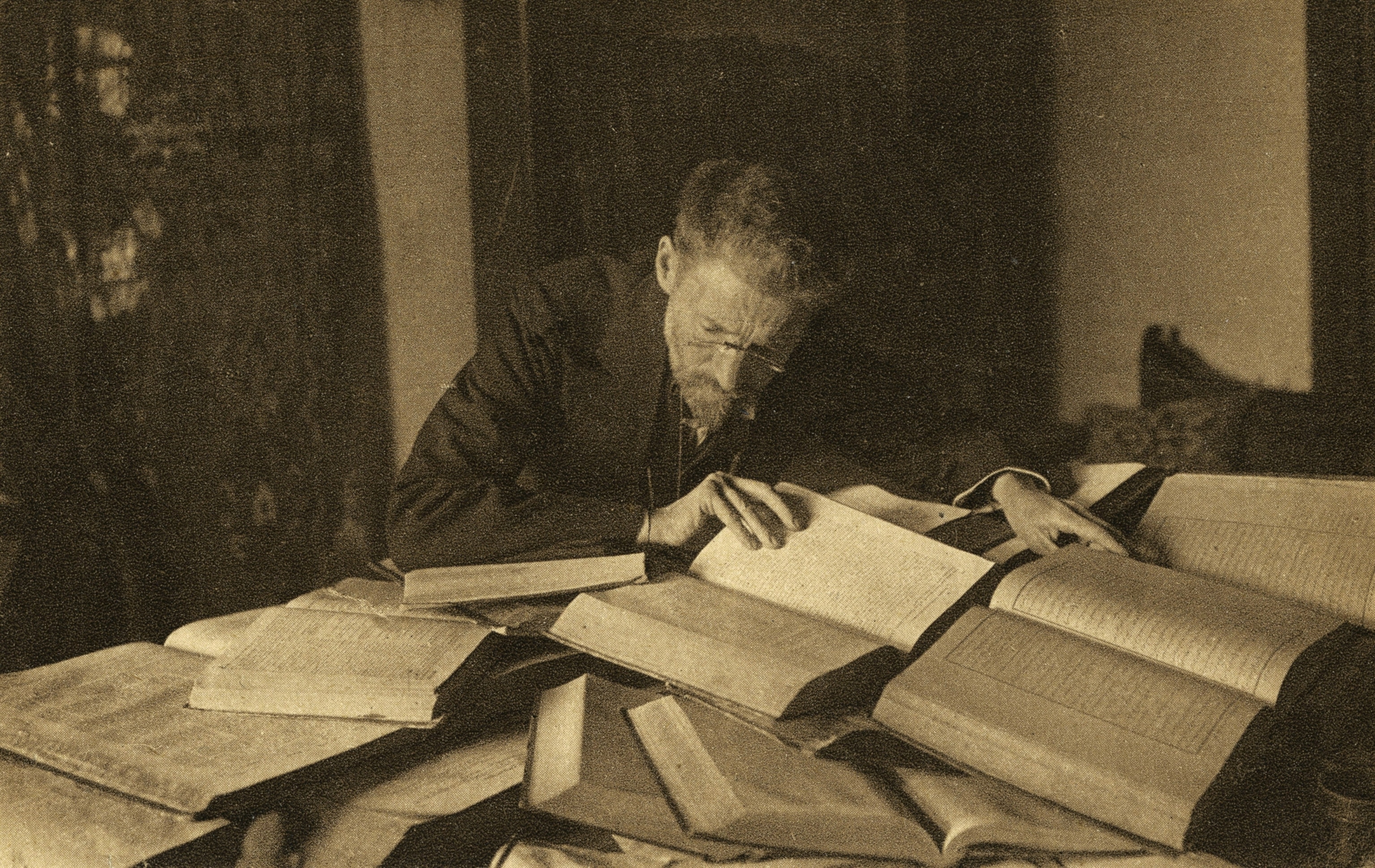 Eliezer Ben-Yehuda reads from one of the dozens of books laying open in a mound on his desk.