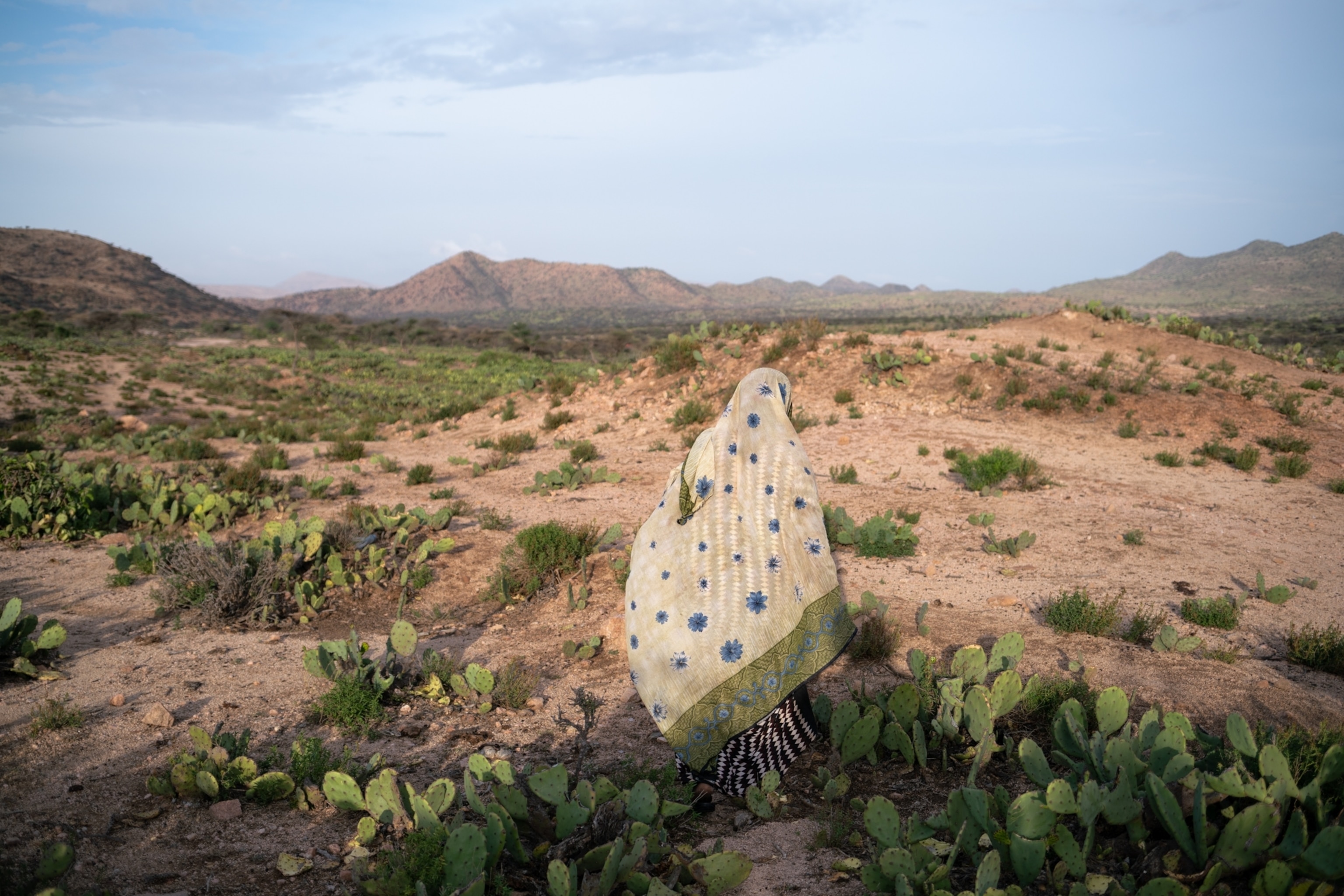 a woman walking away in a headscarf with colors that match the surrounding desert