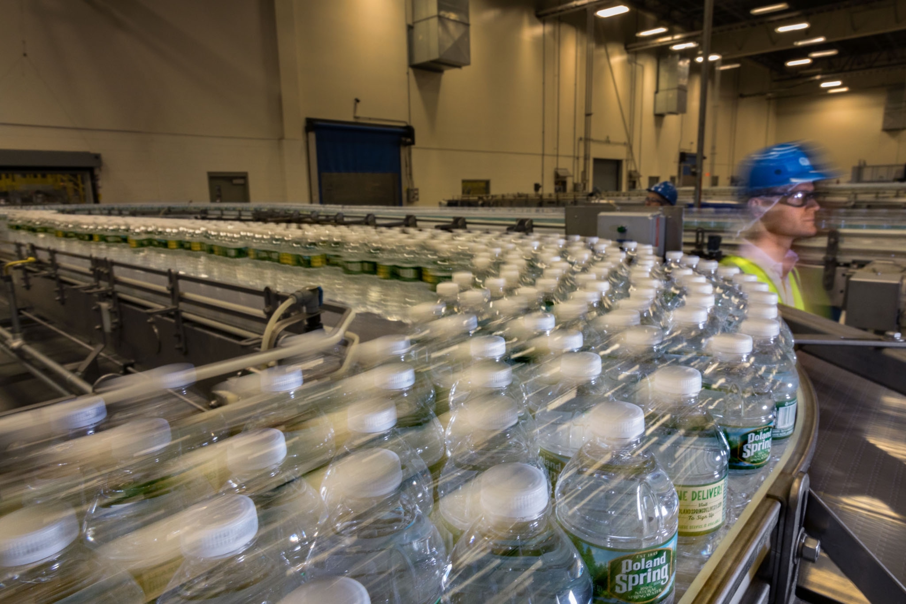 a worker inside a factory, hundreds of plastic water bottles swoop by