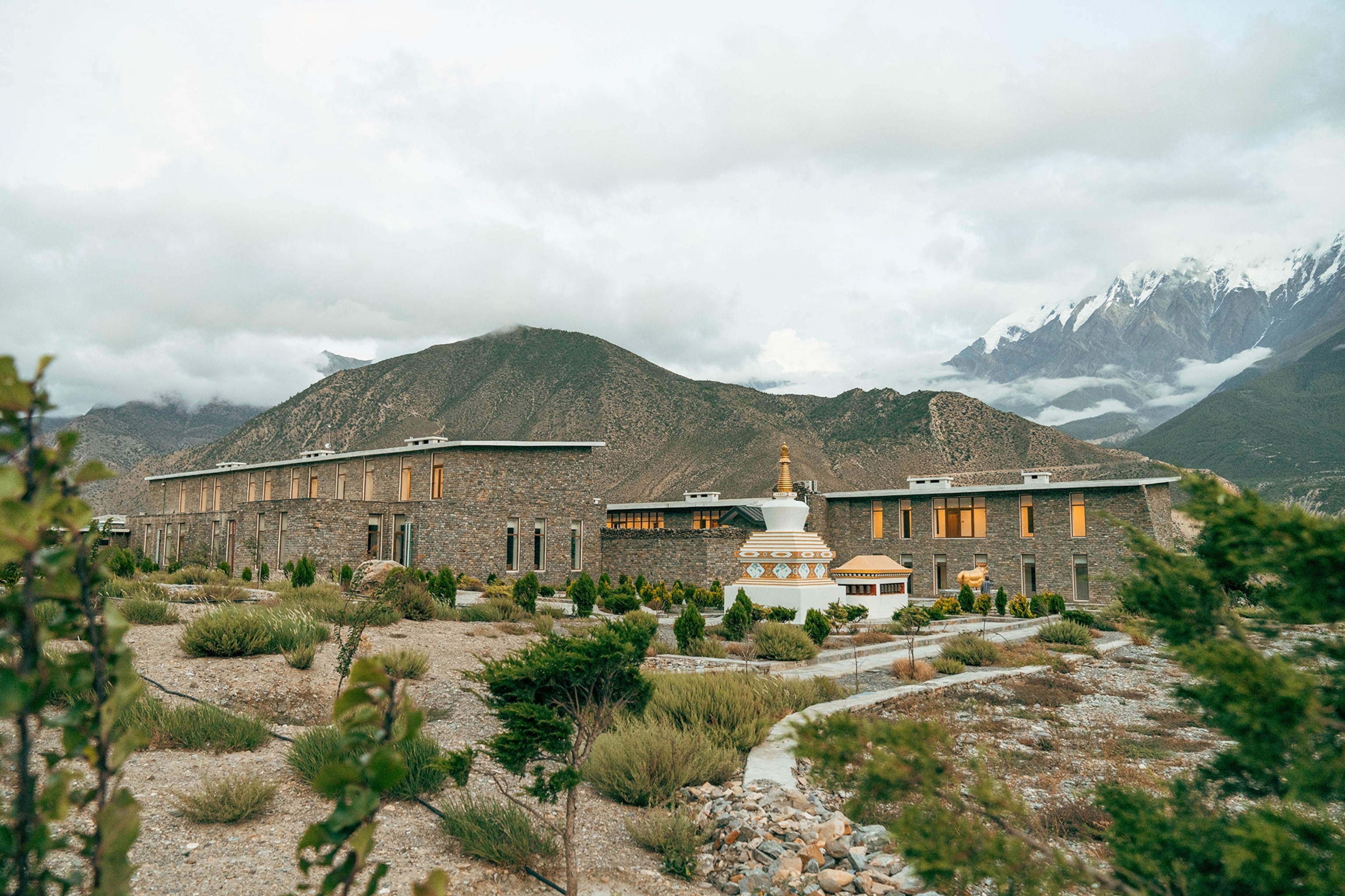 The stone-exterior of the Shinta Mani Mustang resort with a garden in the front and mountains in the background.