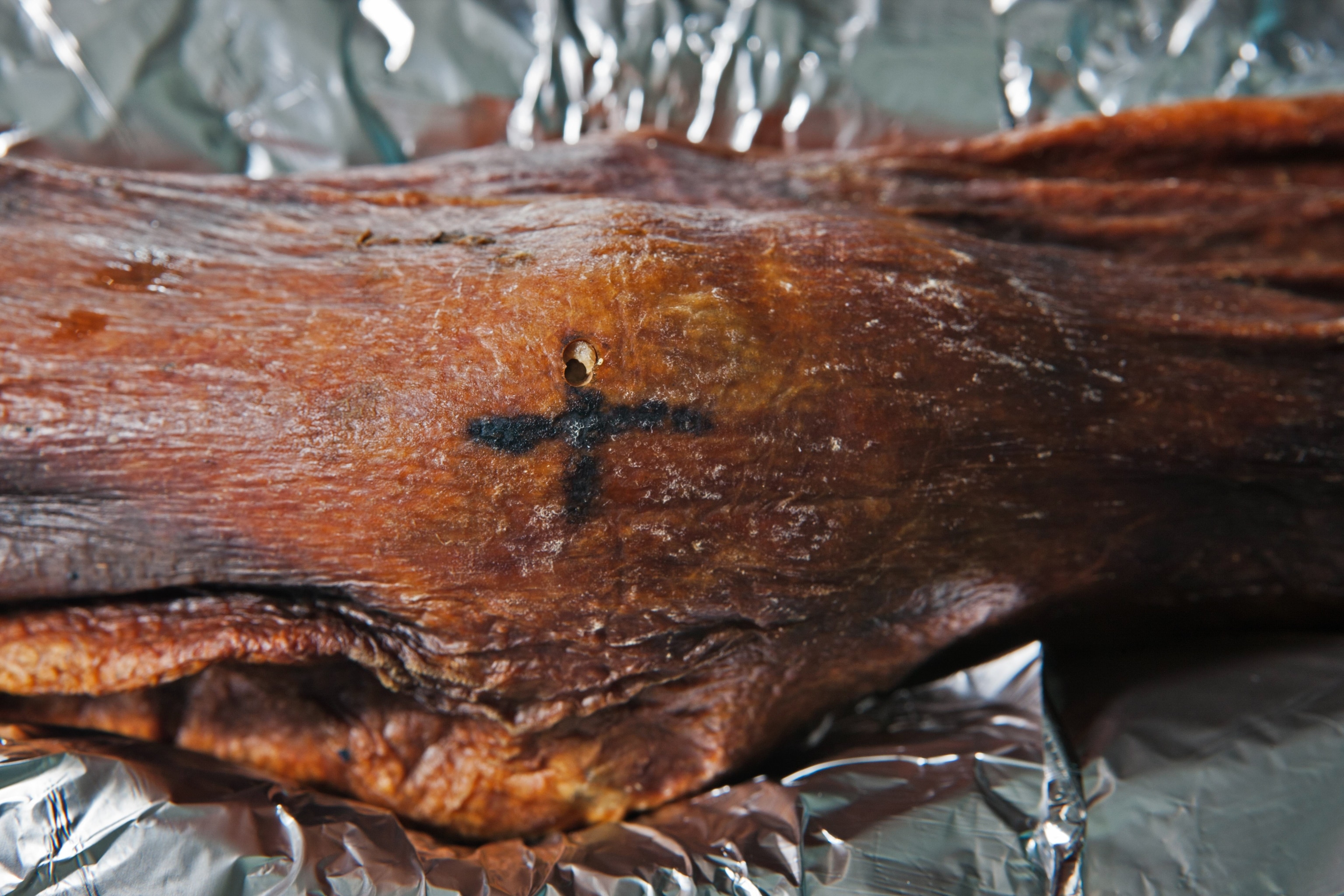 Near the Iceman's knee, a cross-shaped tattoo still stands out on his leathery skin.