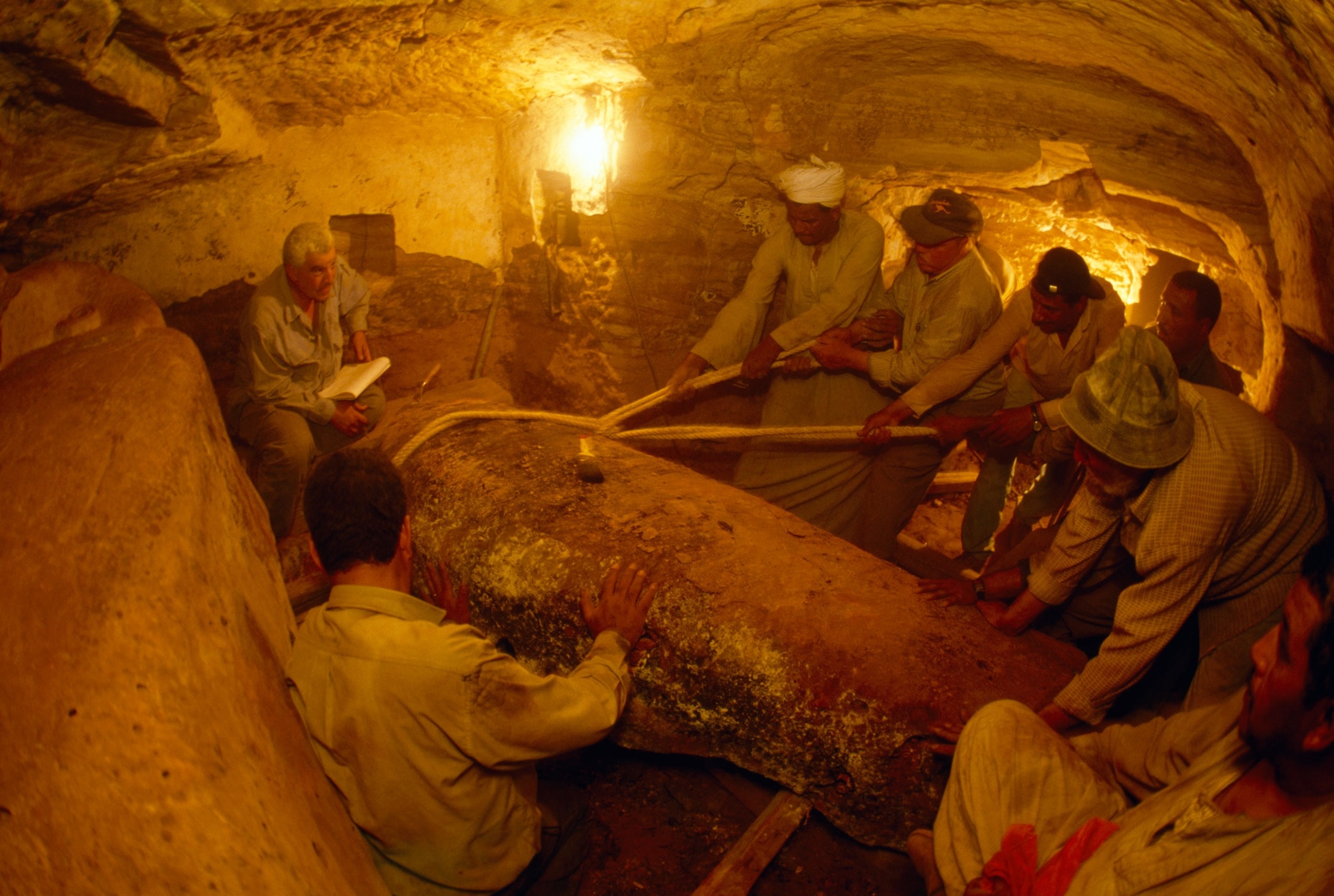 Workers use heavy ropes to pull aside the top to a second sarcophagus made of a labaster.