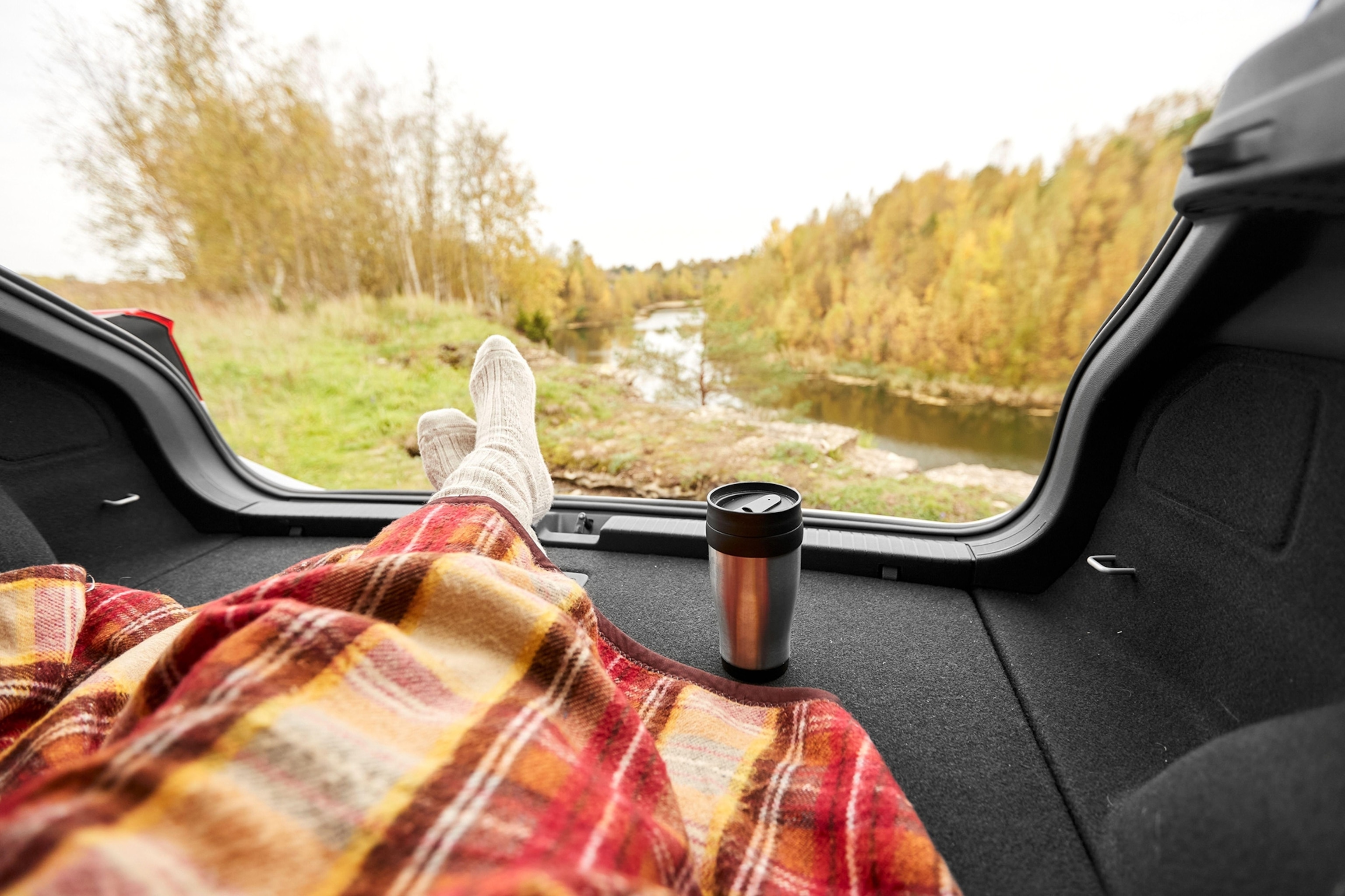 Legs under a blanket with a silver travel mug with a lid.