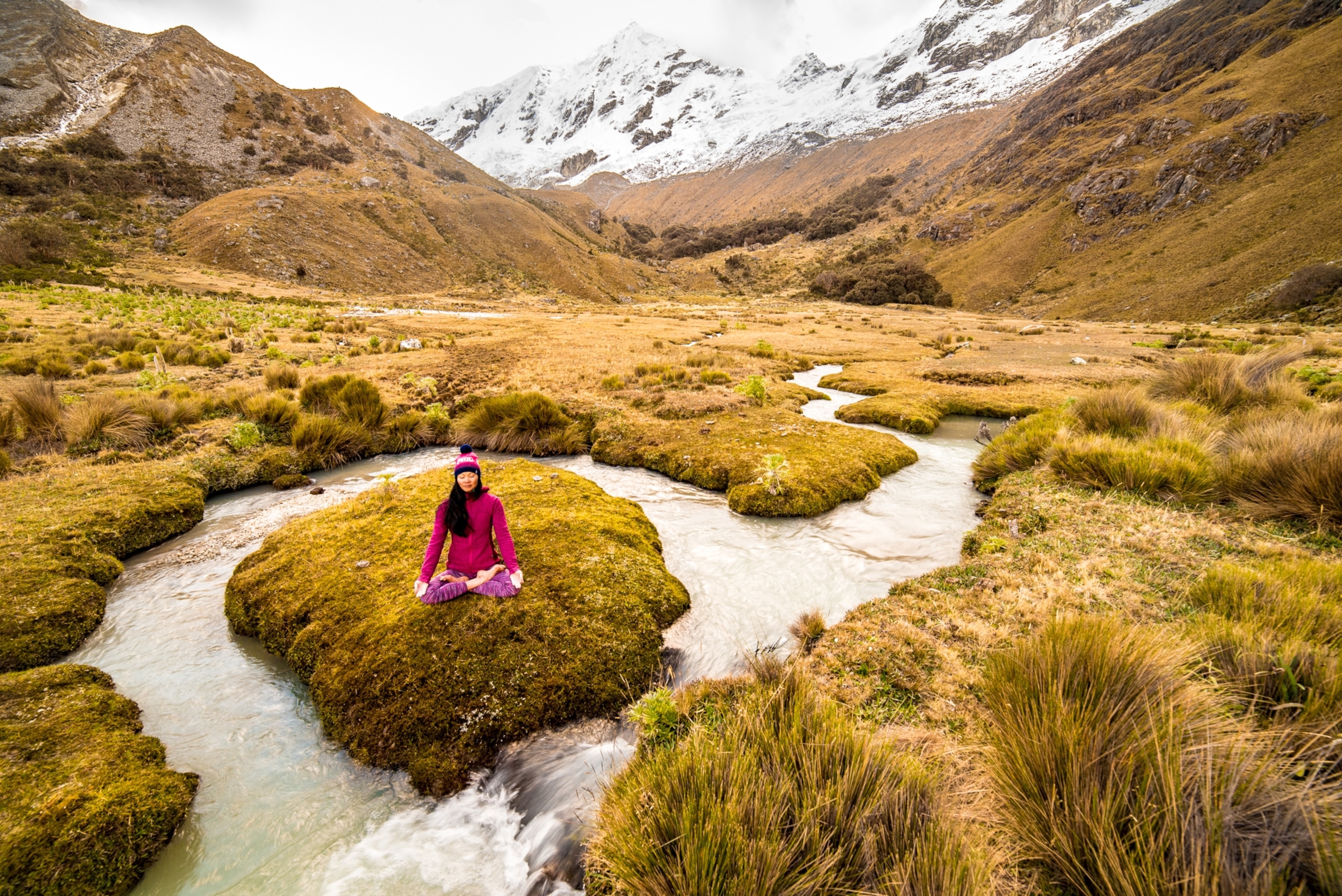 A woman sitting crosslegged as she meditates on tiny islet set in a mountain valley stream.