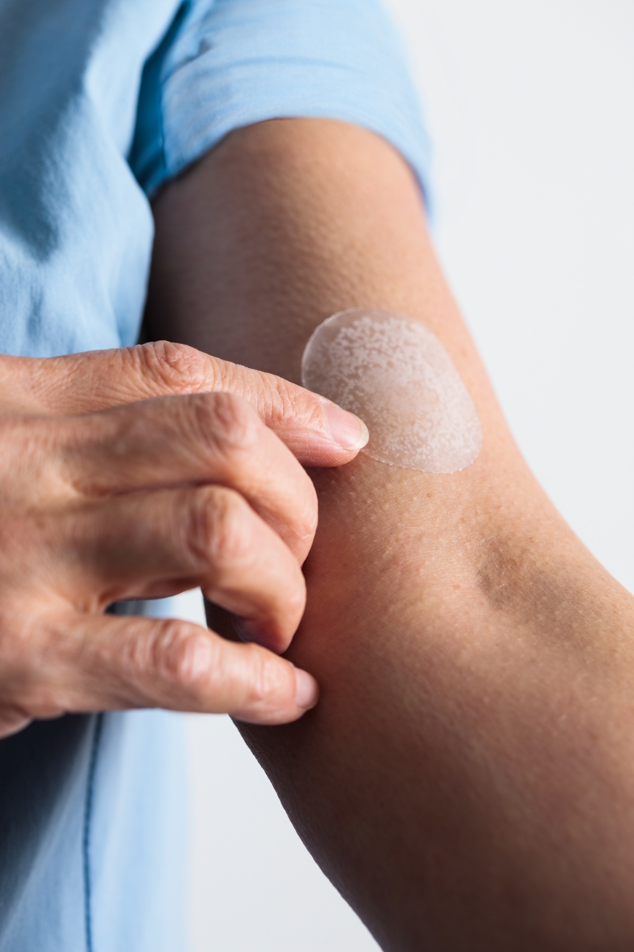A close up view of a woman placing a medicated transdermal patch on her bicep