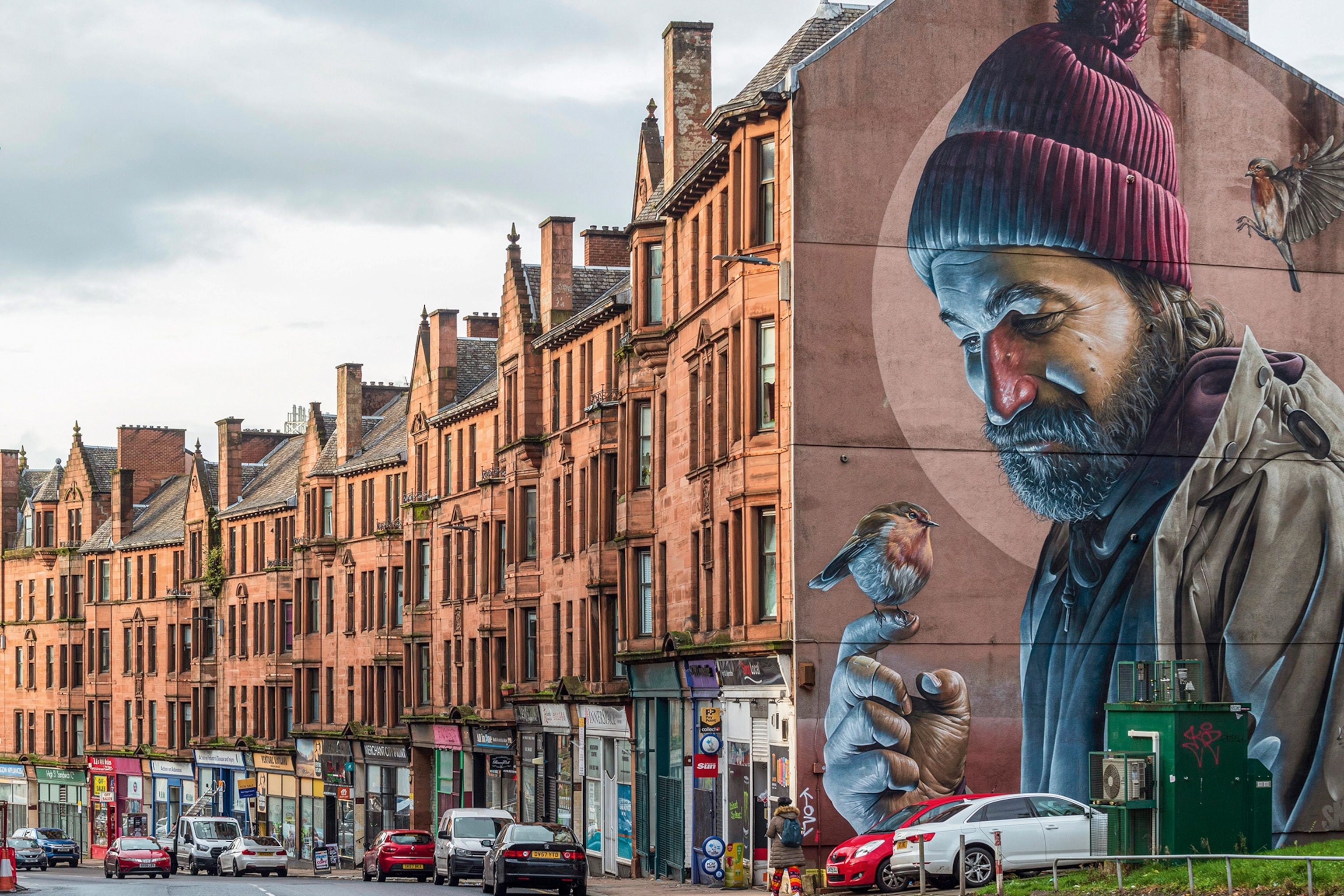 A densely housed street with a mural depicting a bearded man on the facing side of the end house.