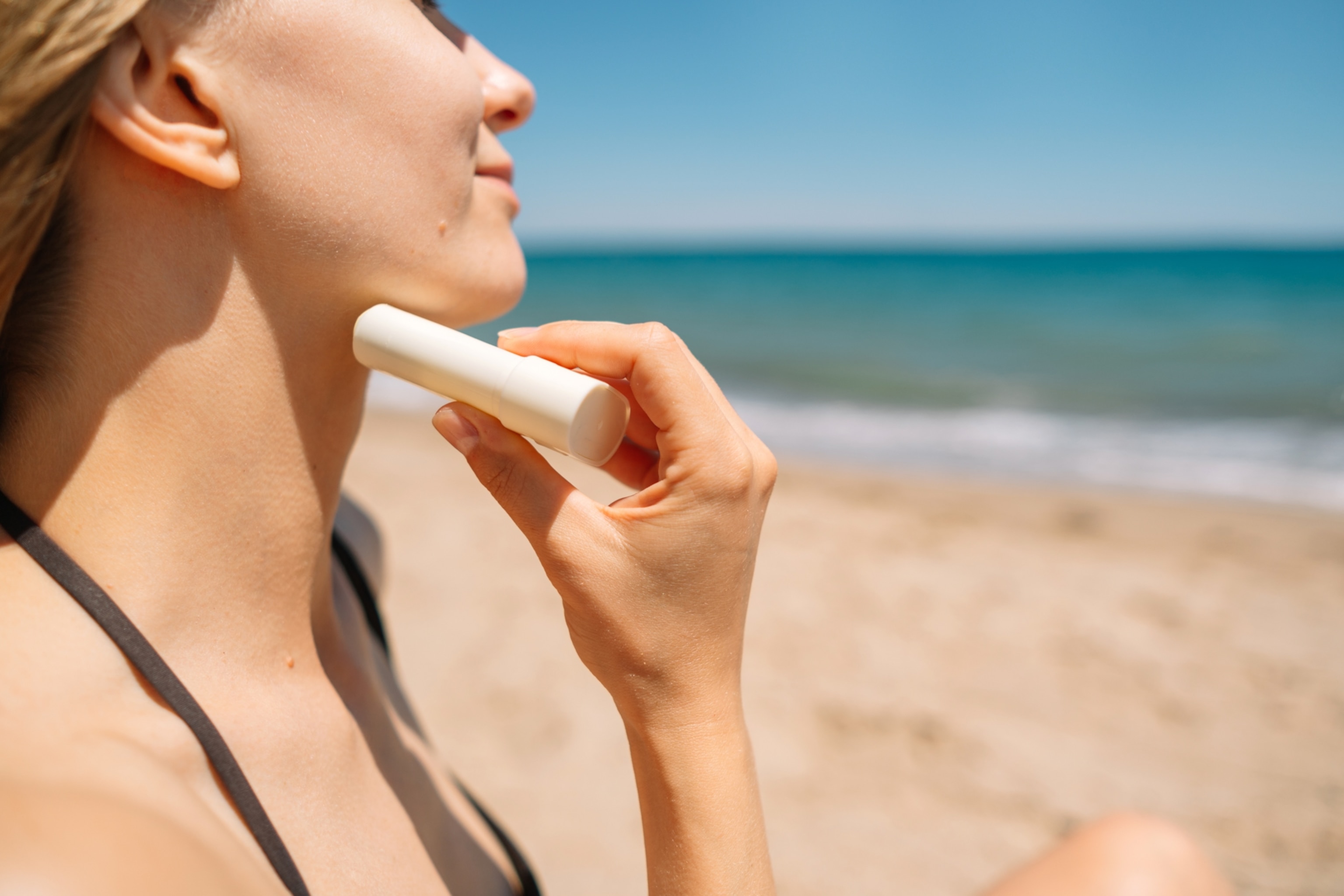 A close-up view of a woman applying sunscreen to her neck using an applicator similar to a stick of deodorant.